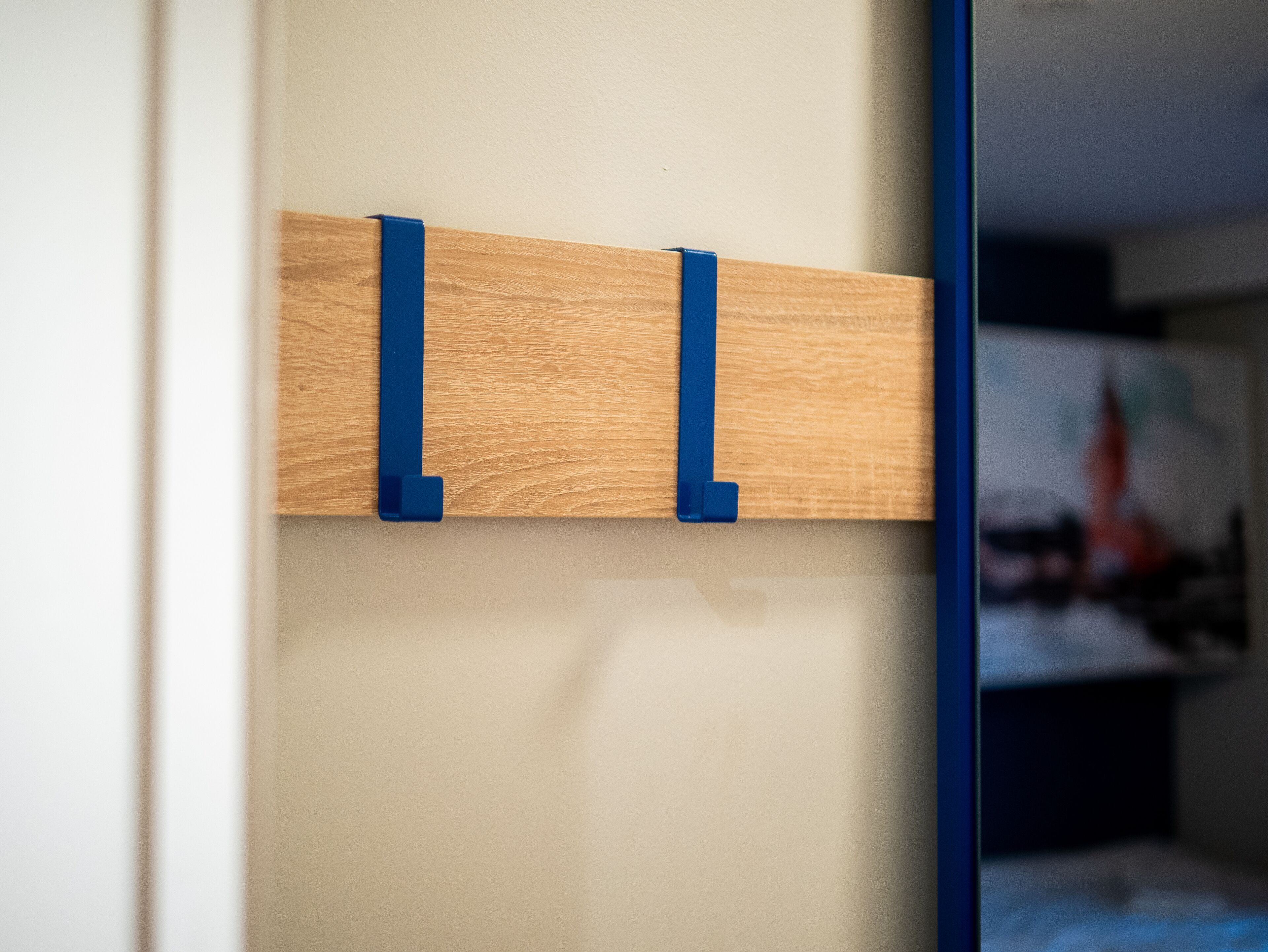 A wooden wall-mounted shelf with two blue clips.
