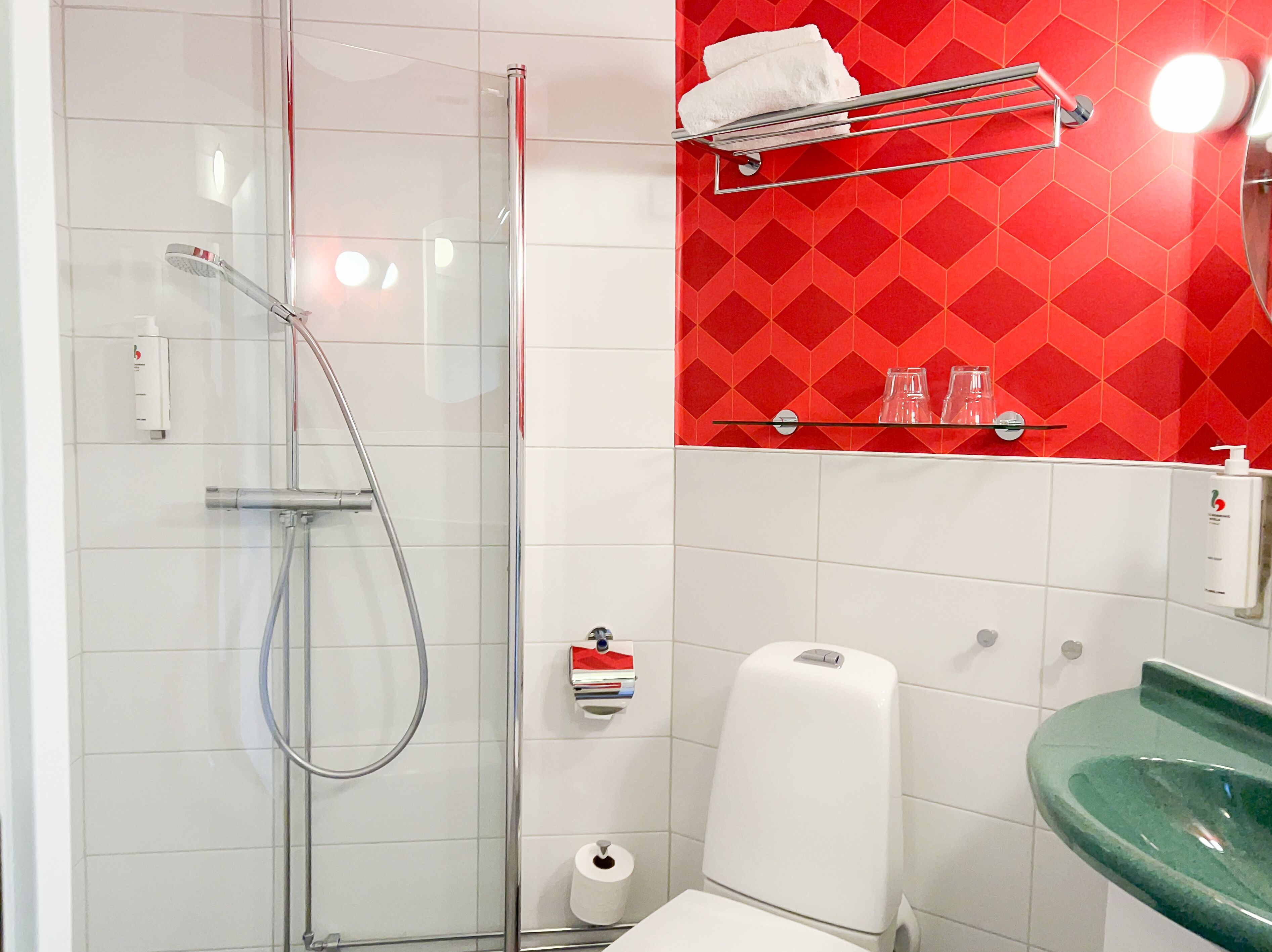 Un bagno moderno con box doccia in vetro, un water bianco, un lavandino verde e una parete con decorazioni rosse.