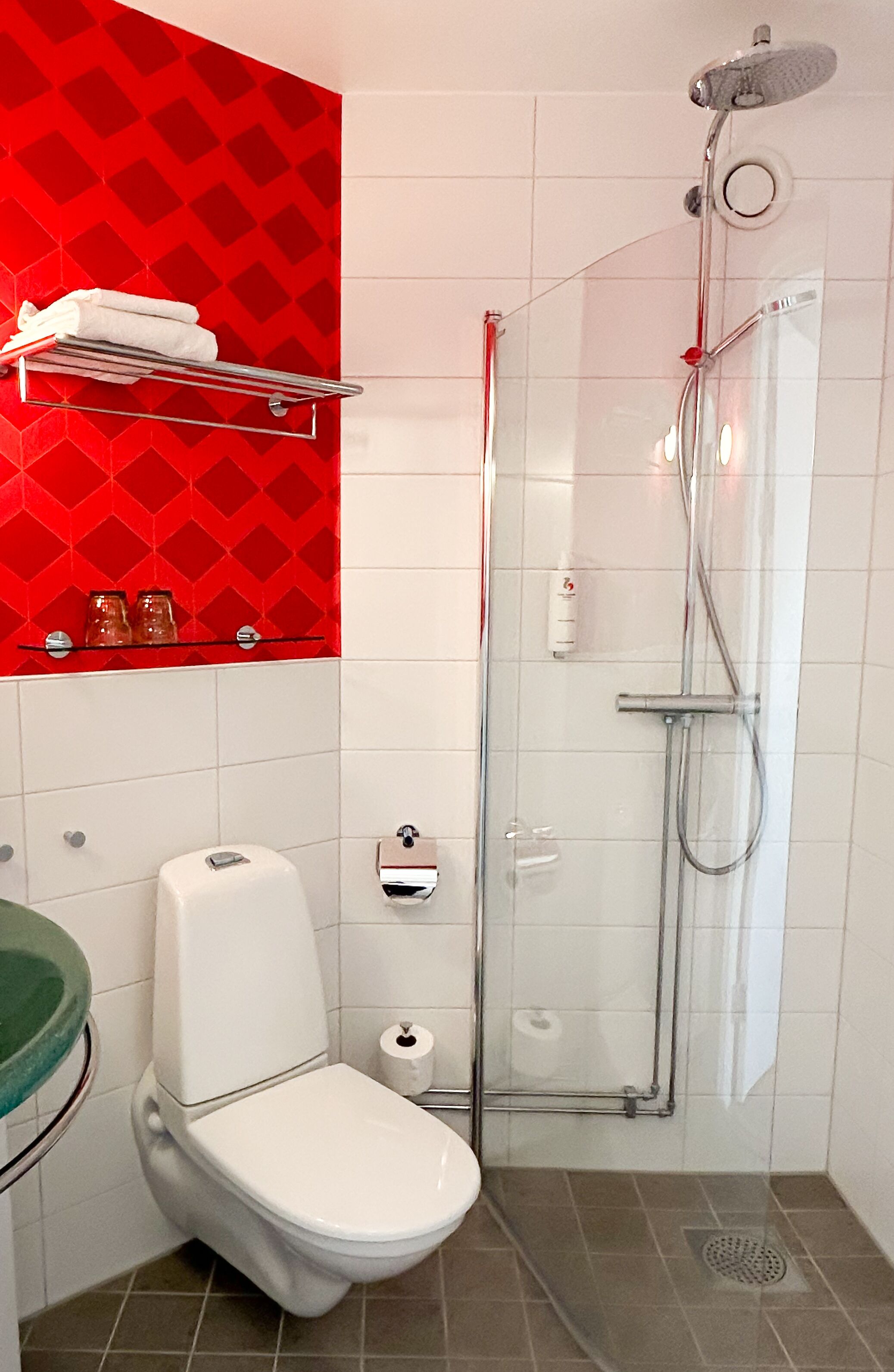 Ein modernes Badezimmer mit einer gläsernen Duschkabine, einer weißen Toilette und einer roten Wand mit Muster.