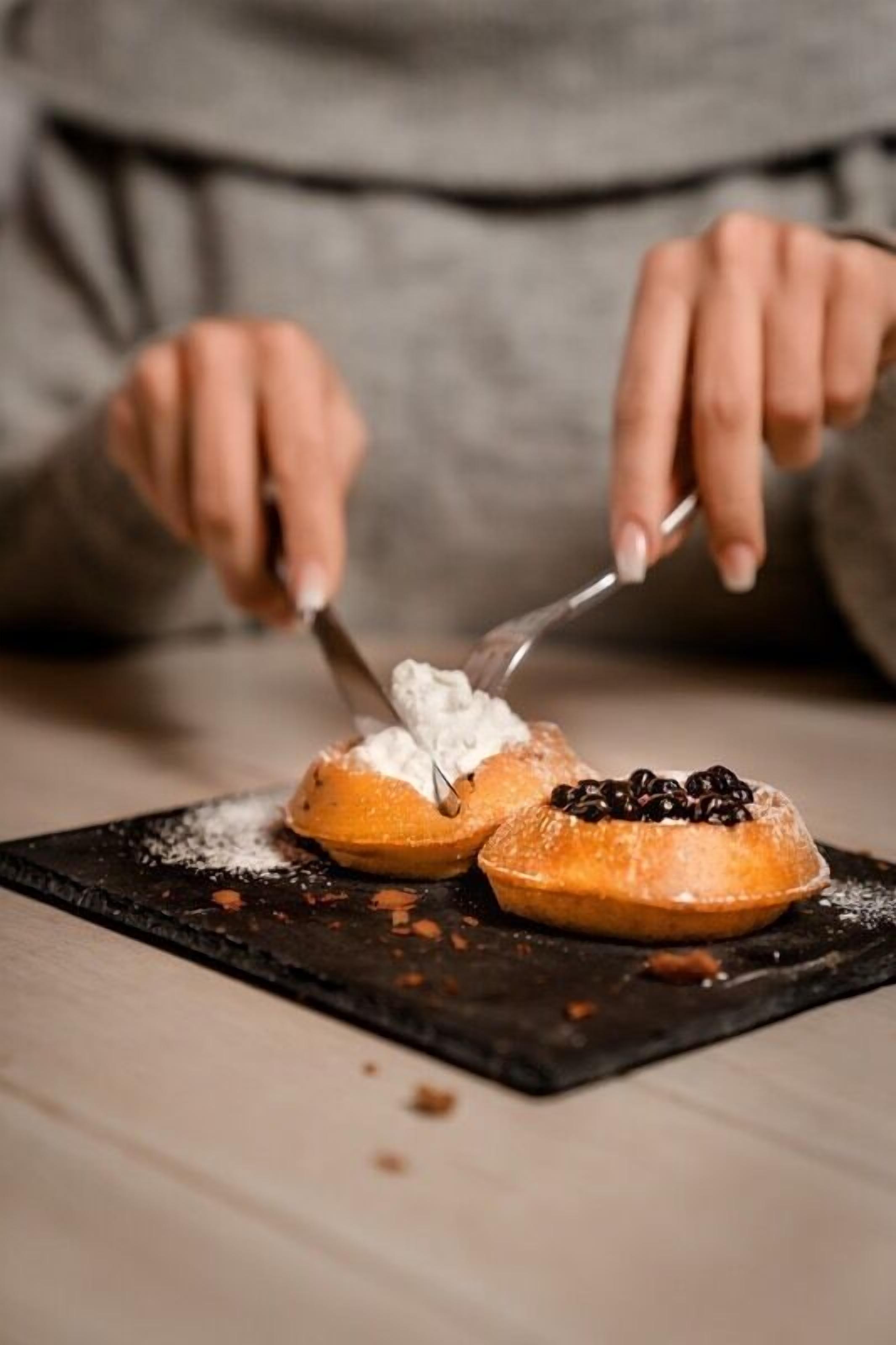 A person serving a dessert with powdered sugar and berries on a black plate.