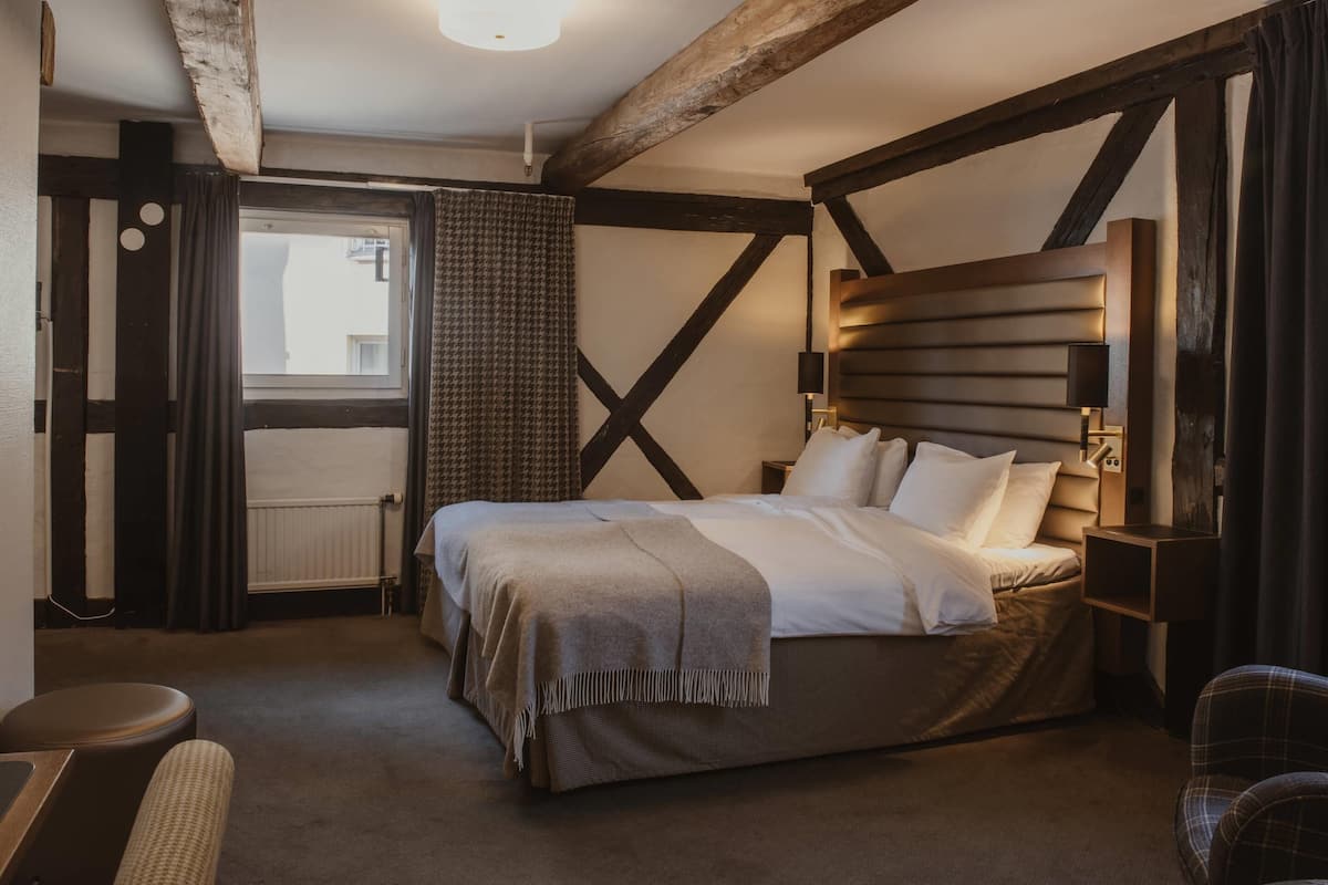 A bedroom with a large bed, a wooden headboard, a bedside table, and a chair.