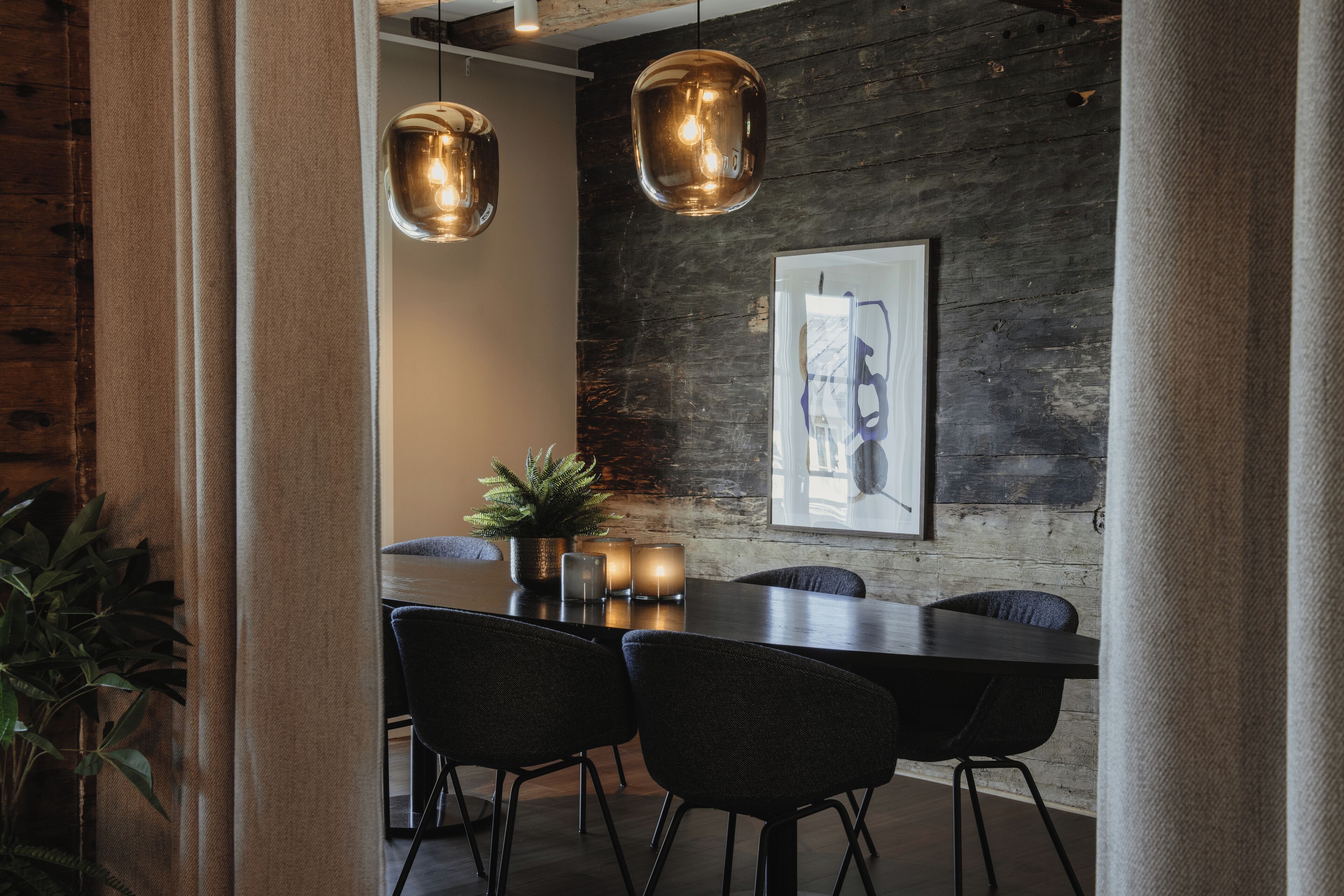 Un comedor moderno con una pared de madera oscura, una obra de arte enmarcada y lámparas colgantes.