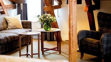 A cozy attic bedroom with exposed wooden beams, a plaid sofa, a chair, and a small table with a vase.