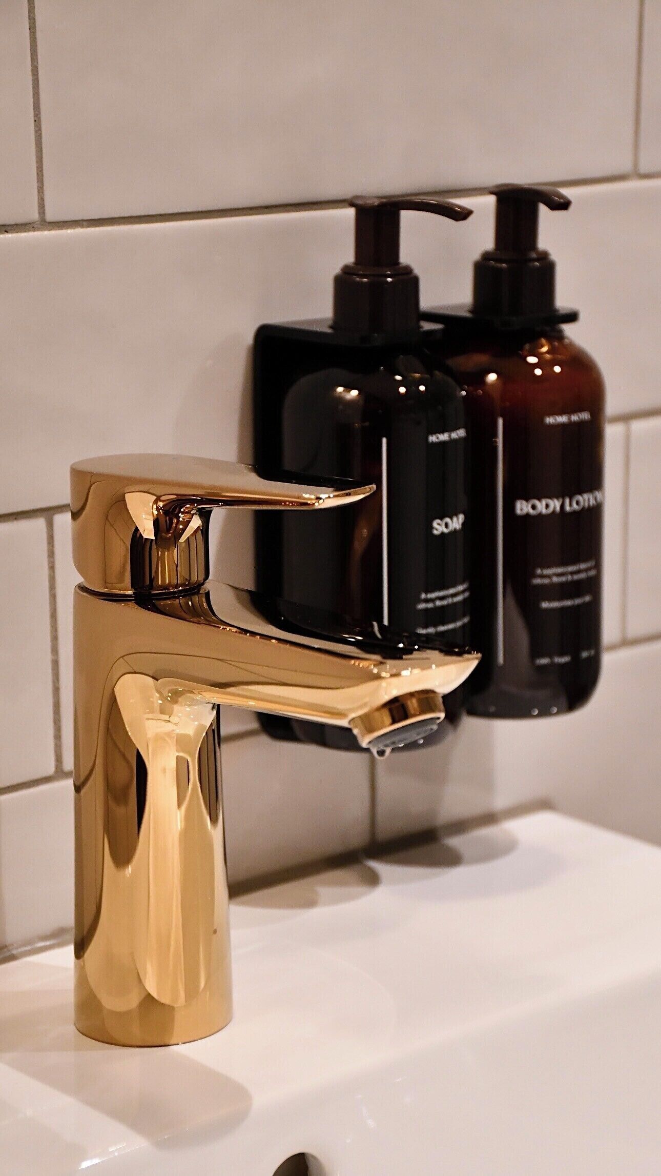 Un baño con grifo dorado, dispensador de jabón negro y dispensador de loción corporal negro.
