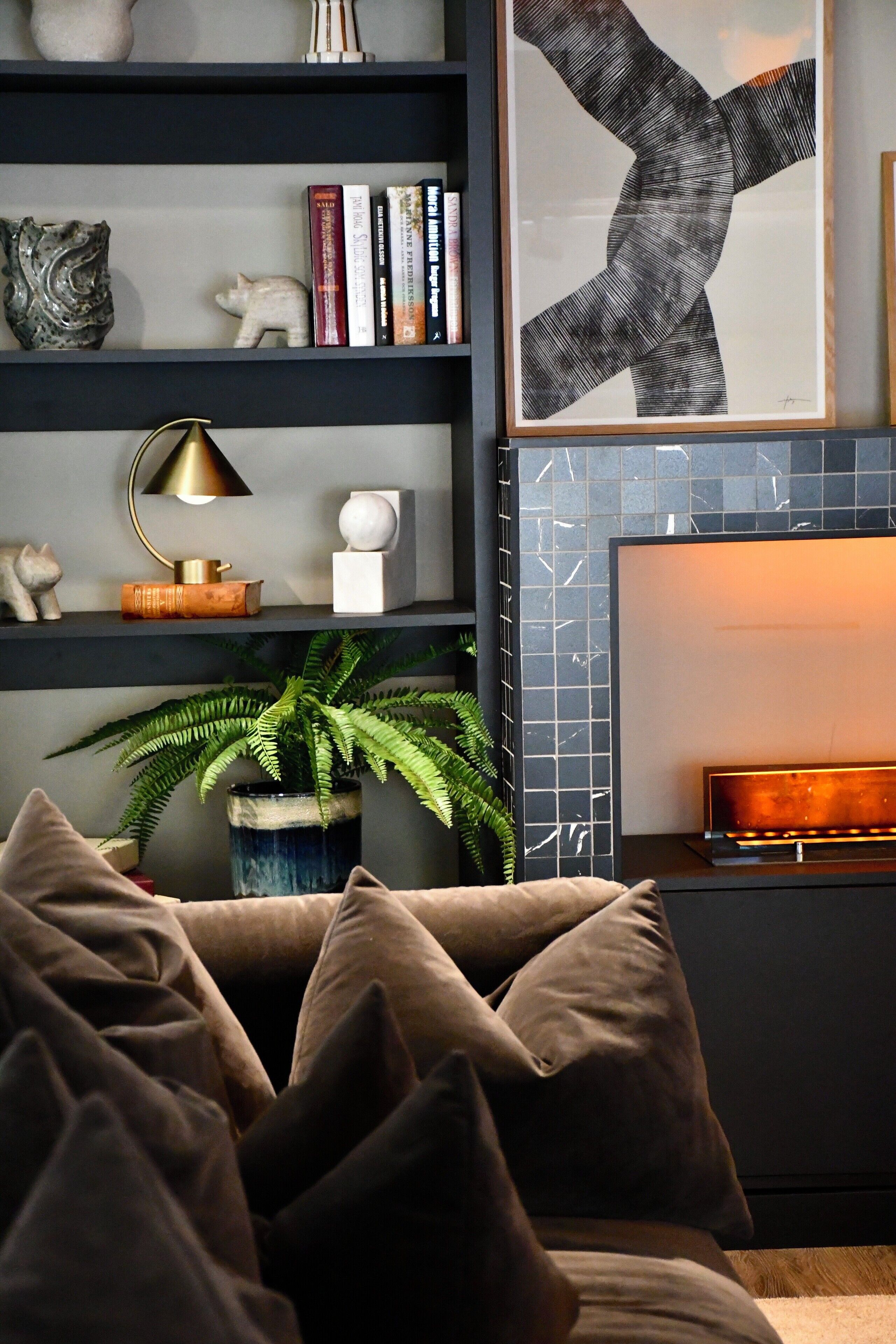 A modern living room with a dark wood bookshelf, a large abstract painting, a potted fern, and a cozy fireplace.