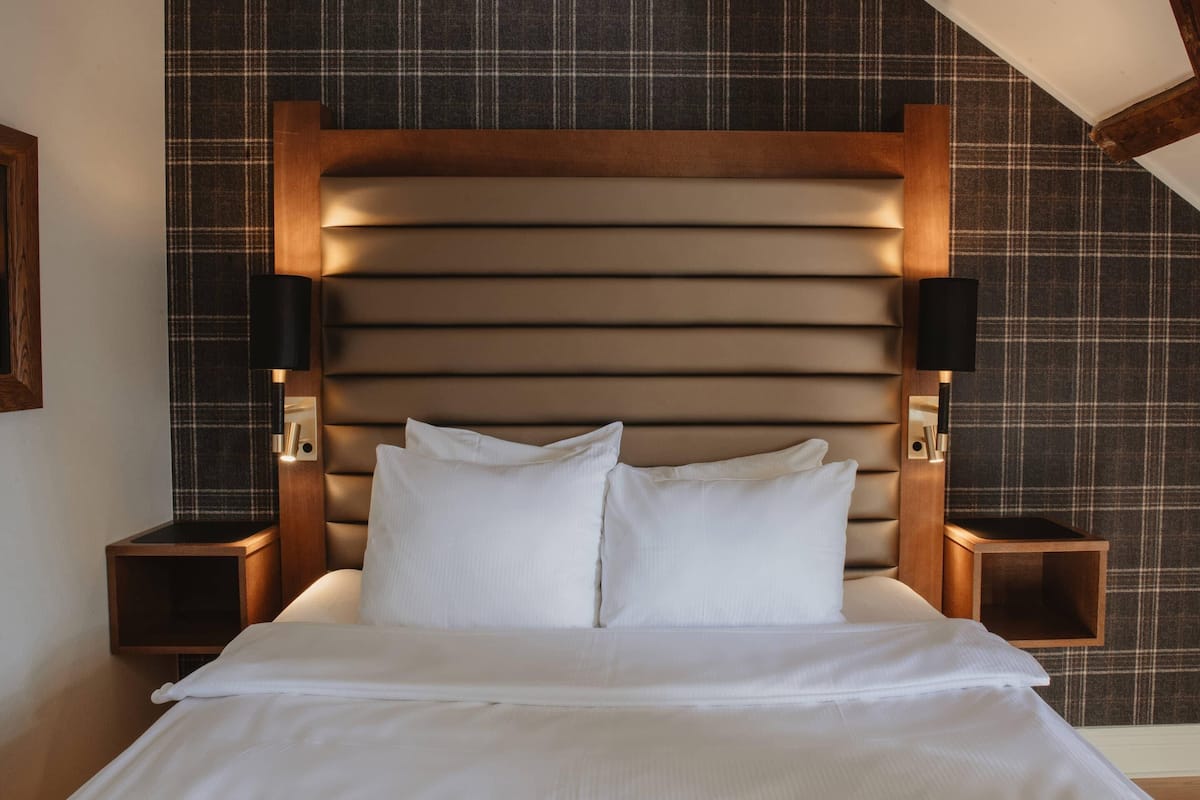 A neatly made bed with white linens, a wooden headboard, and two bedside tables with lamps.