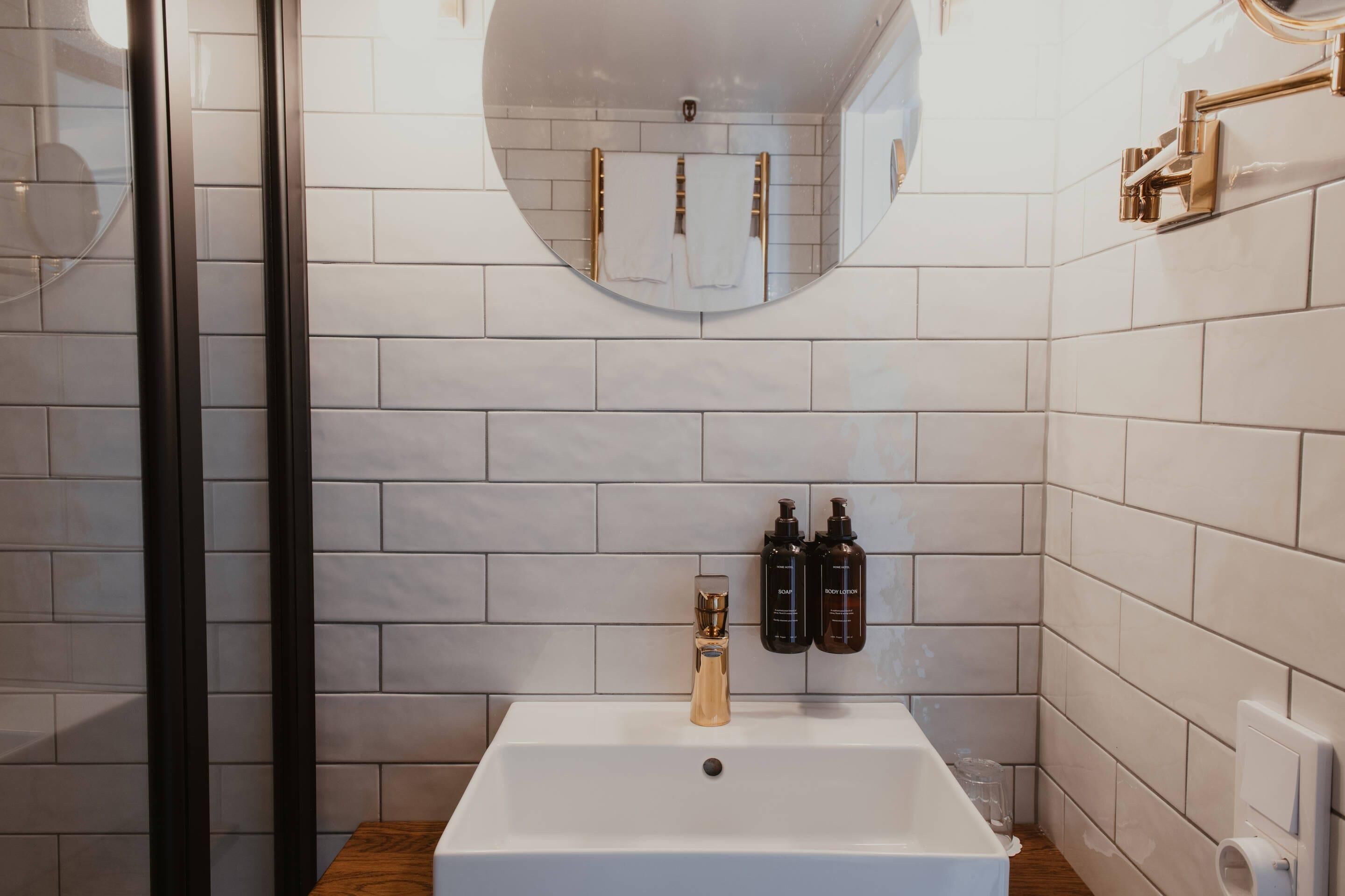 A bathroom with a white sink, two bottles of shampoo, a mirror, and a glass shower enclosure.
