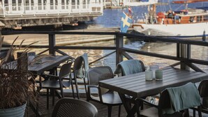 Terraza de madera con mesas y sillas, con vistas a un puerto deportivo lleno de barcos y un barco amarrado.
