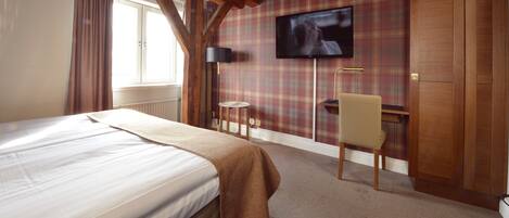 A hotel room with a bed, a television mounted on the wall, a small table, and a chair.