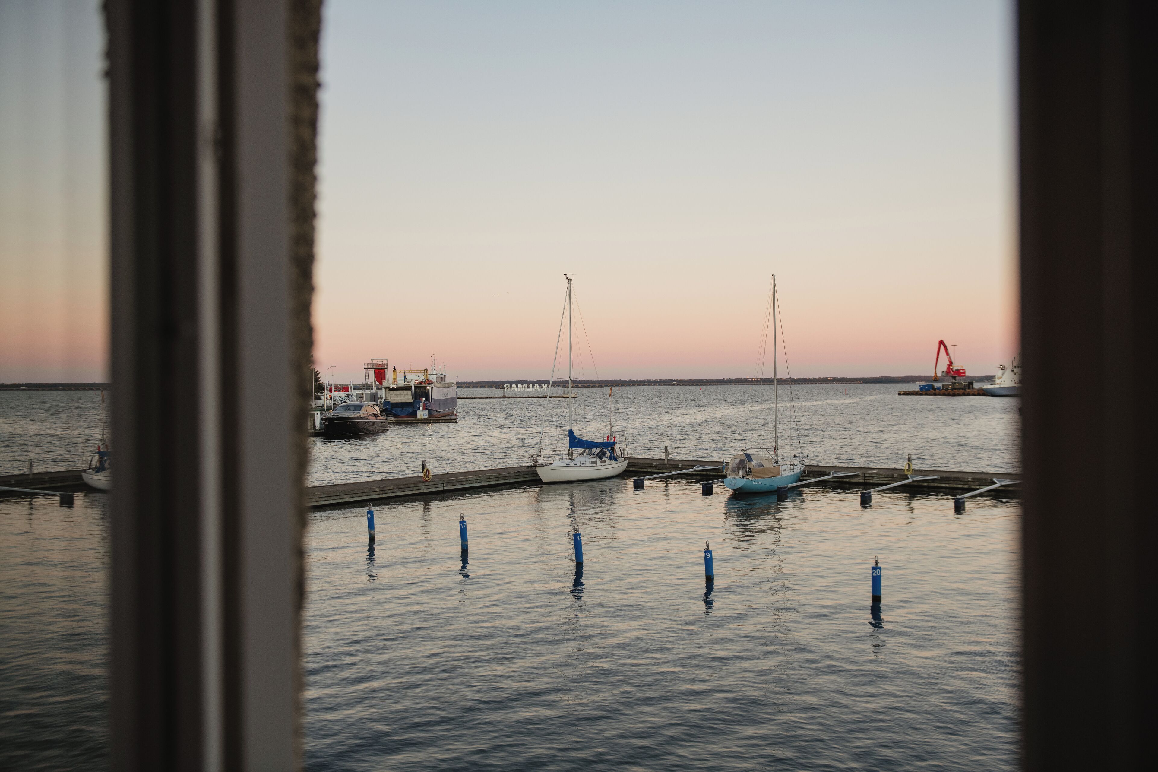 A marina with boats docked at wooden piers, calm water, and a clear sky.