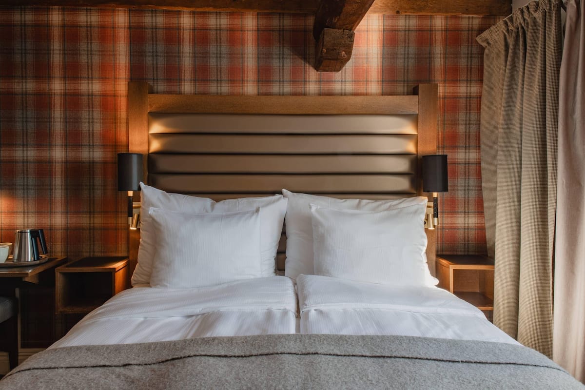 A neatly made bed with white linens, a wooden headboard, and two bedside lamps.