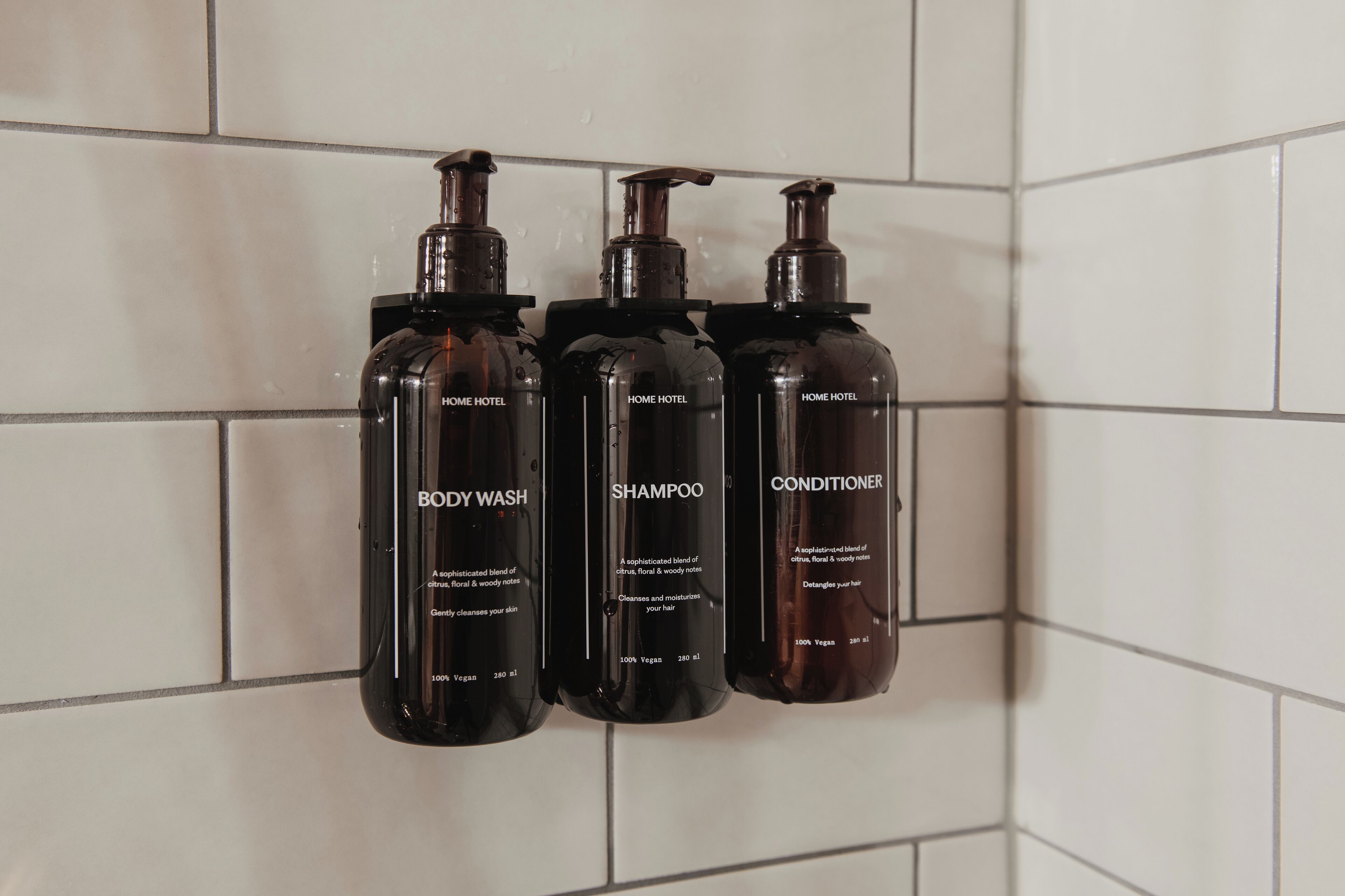 Three black bottles of toiletries on a tiled wall.