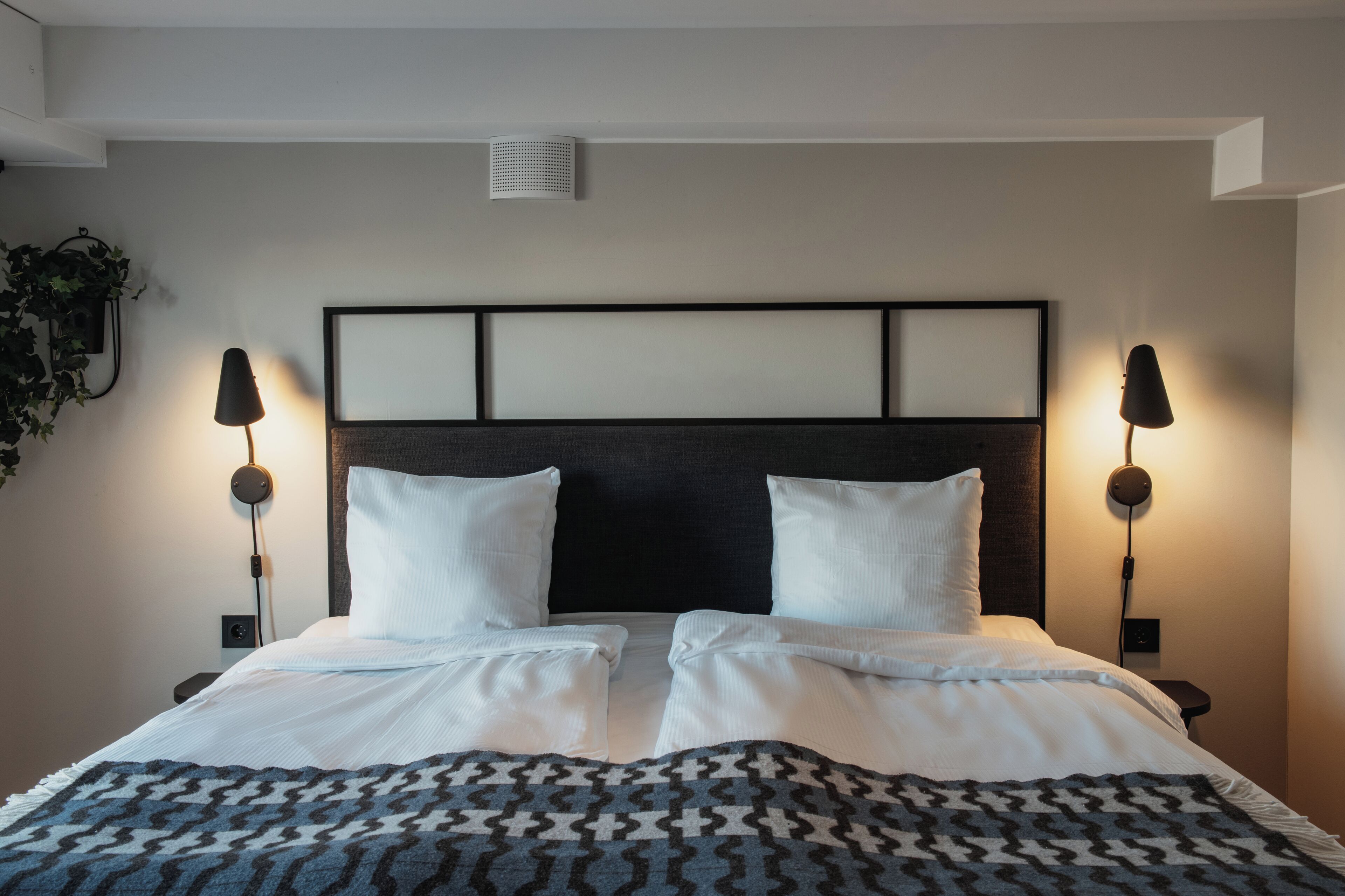 A double bed with a patterned blanket, two bedside lamps, and a headboard with a grid design.