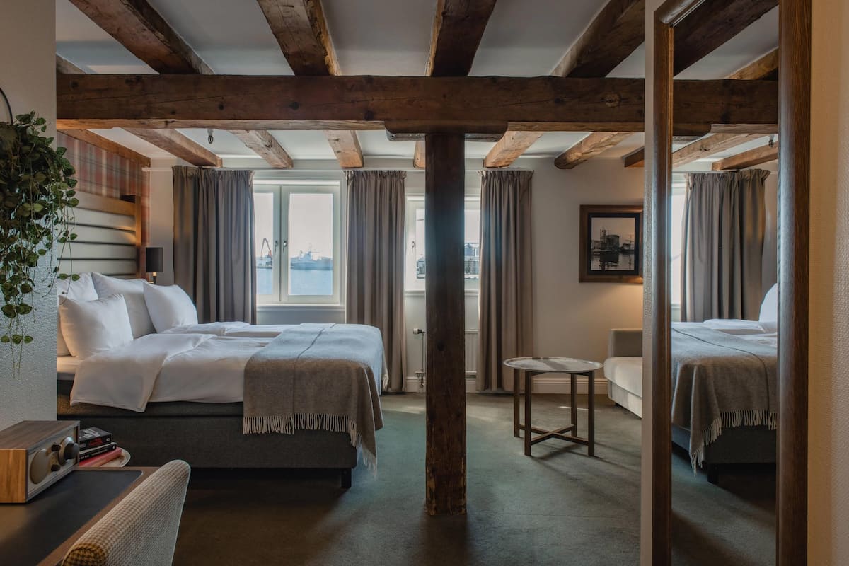 A hotel room with two beds, a small table, a chair, a radio, and a view of the city.