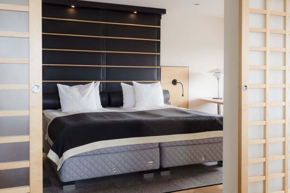 A modern bedroom with a large bed, a bedside table, and a lamp.