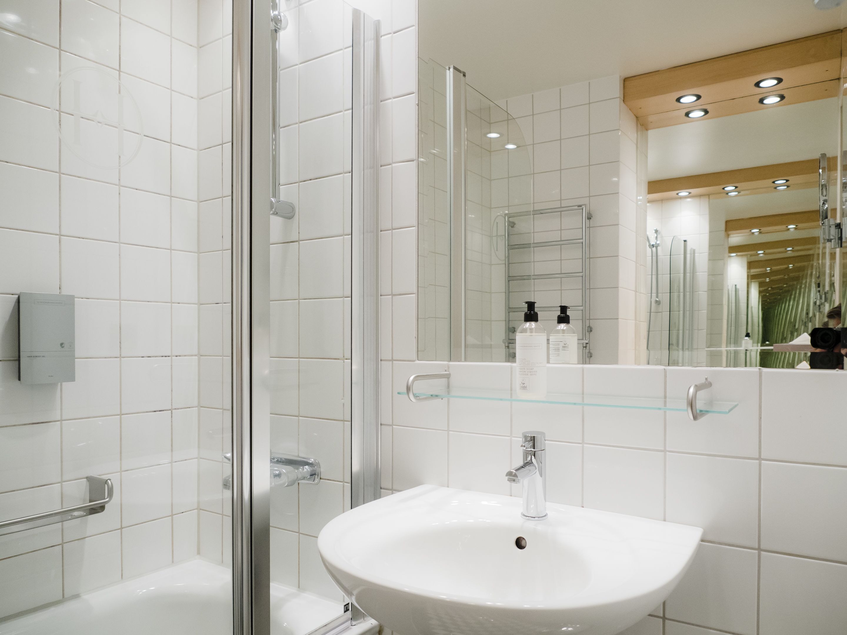 A modern bathroom with a glass shower enclosure, a white sink with a chrome faucet, and a mirror reflecting the room.