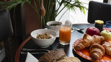 Disposição para o café da manhã com croissants, frutas, um copo de suco de laranja e uma tigela de cereal.