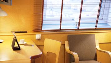 Habitación de hotel con una mesa de madera, dos sillas, una lámpara y un ventanal con persianas.