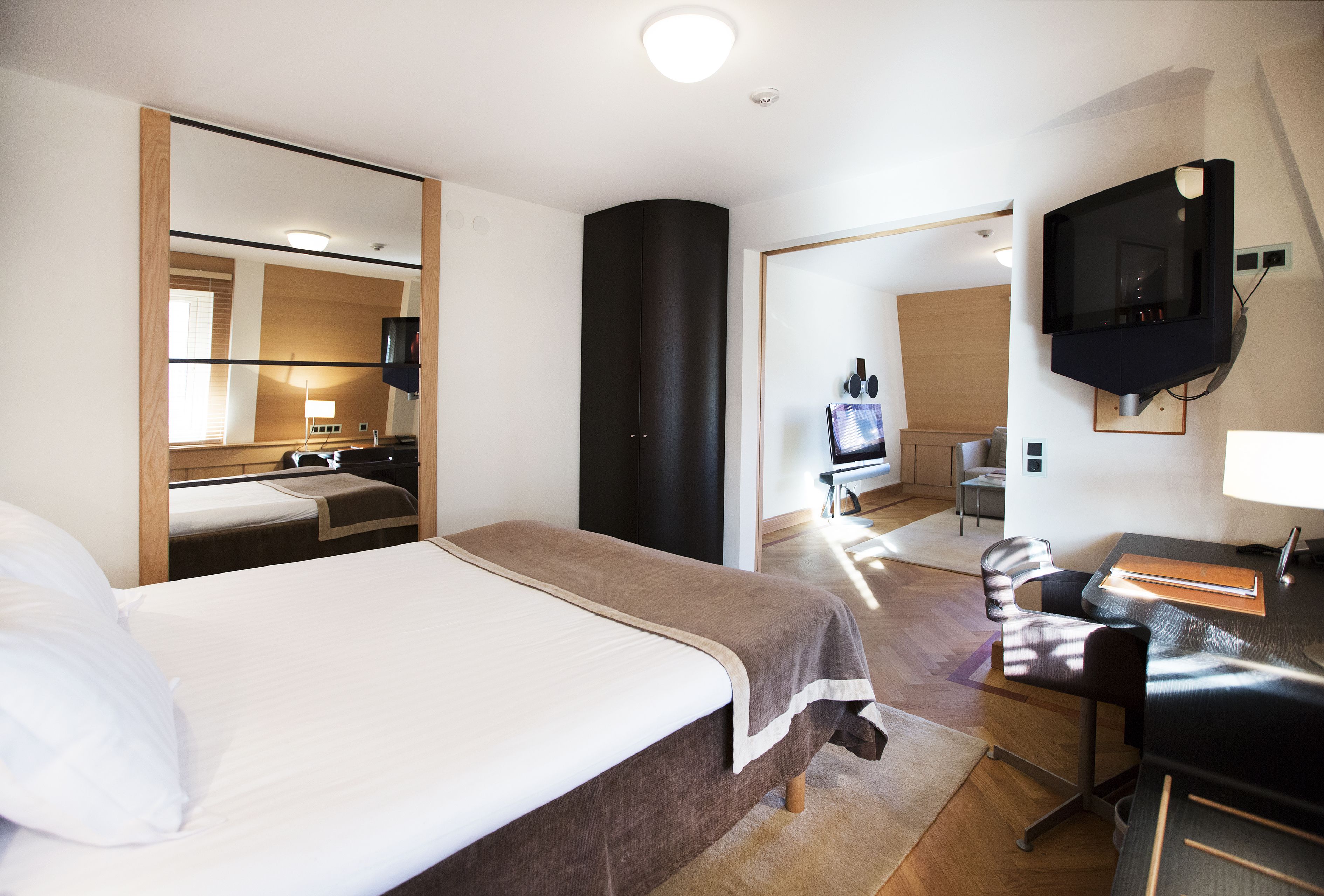Une chambre d’hôtel avec un grand lit, un bureau avec une chaise, un téléviseur fixé au mur et un miroir.