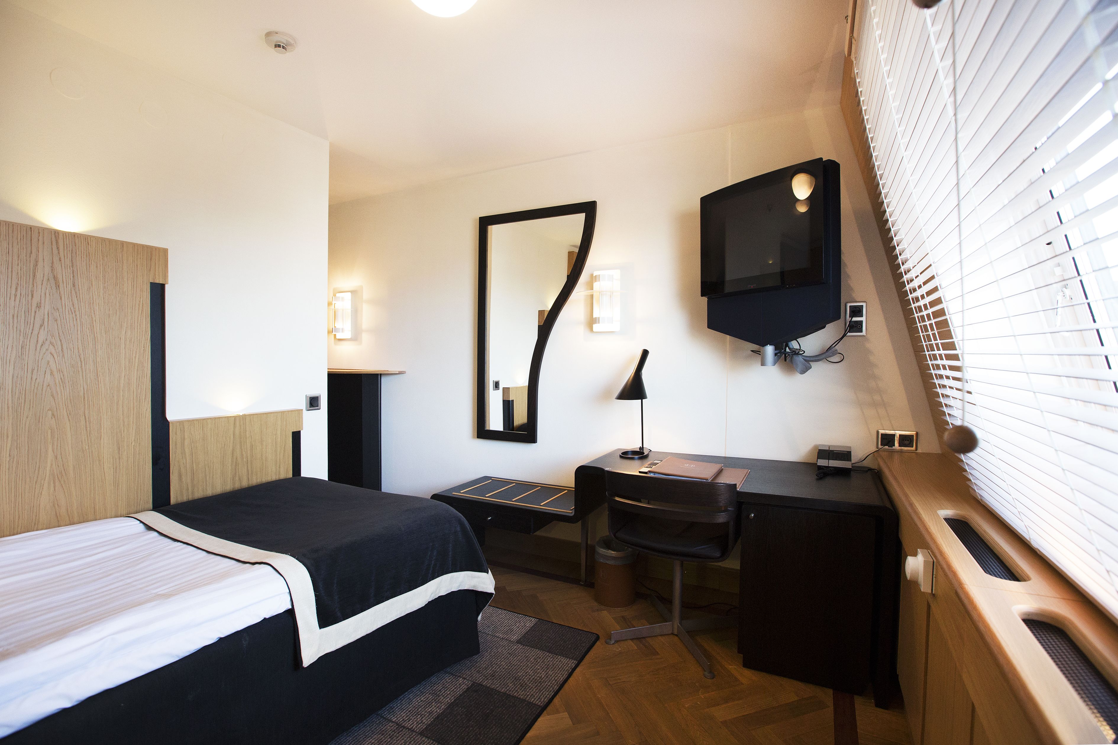 A hotel room with a bed, desk, chair, and a TV mounted on the wall.