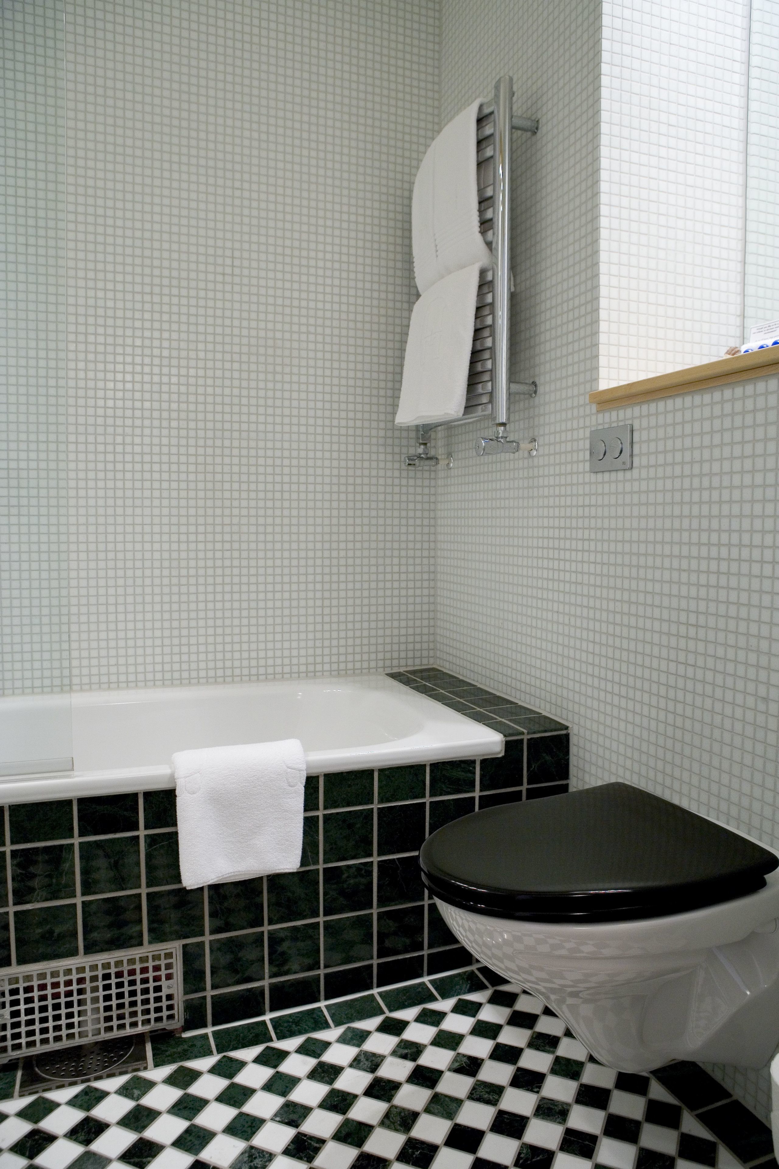 A bathroom with a white bathtub, a black toilet, and a checkered floor.