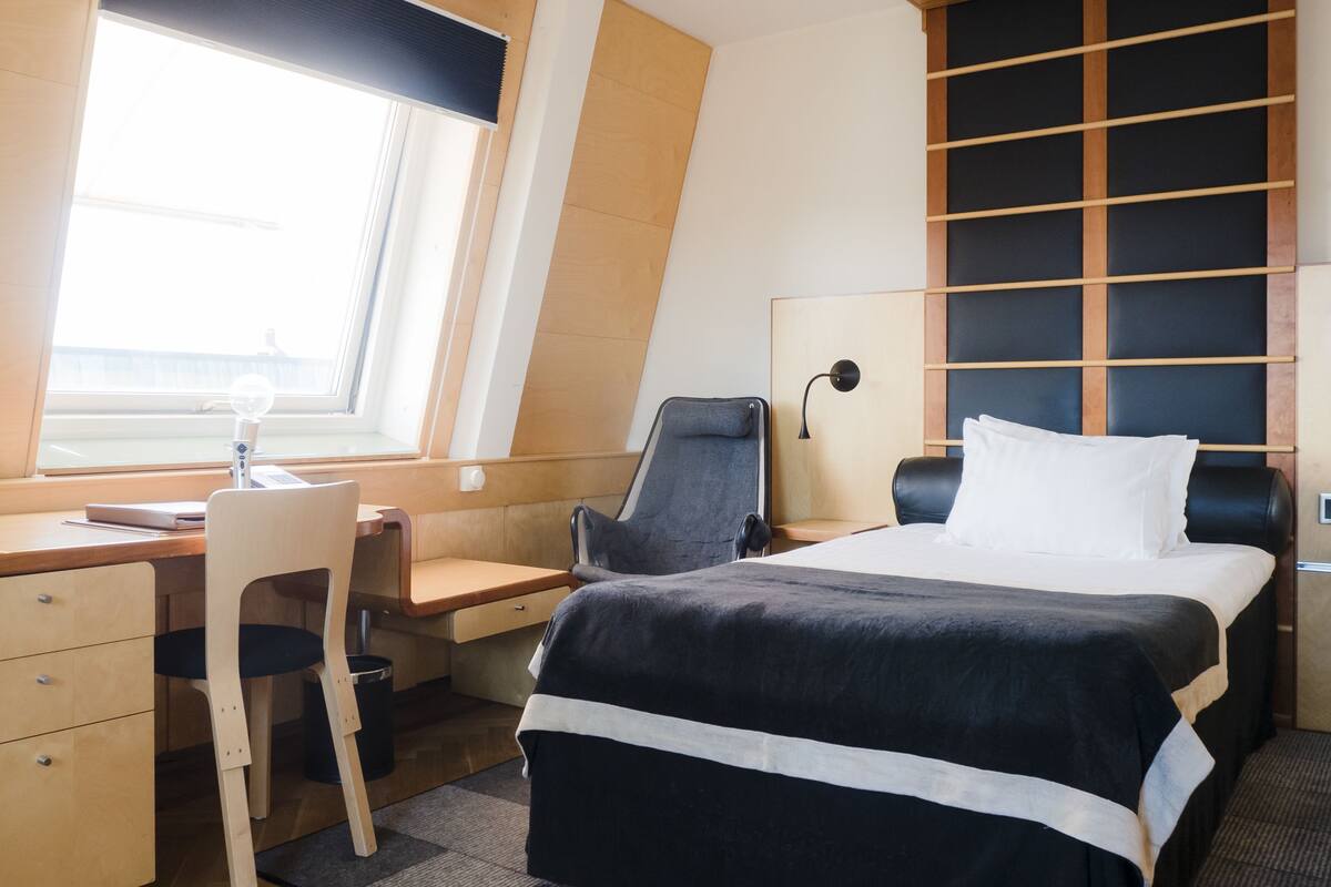 A modern hotel room with a desk, chair, bed, and a large window.