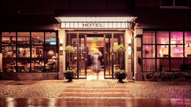 A hotel entrance with a glass facade, a sign reading "HOTEL", and a neon sign in the background. - Best Western Plus Hotel Noble House (Malmö)