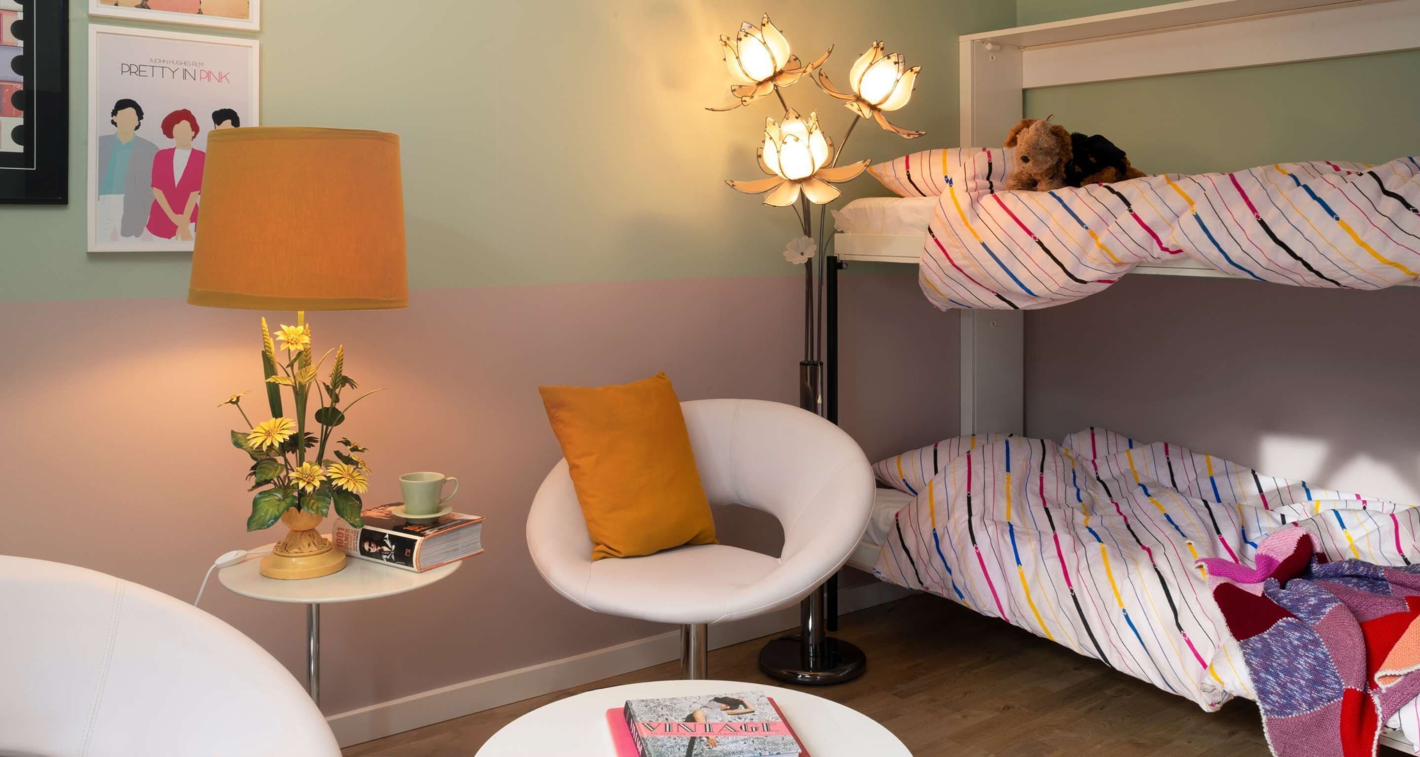 Une chambre confortable avec un lit superposé, une chaise blanche, une table de chevet avec une lampe et un tableau encadré au mur.