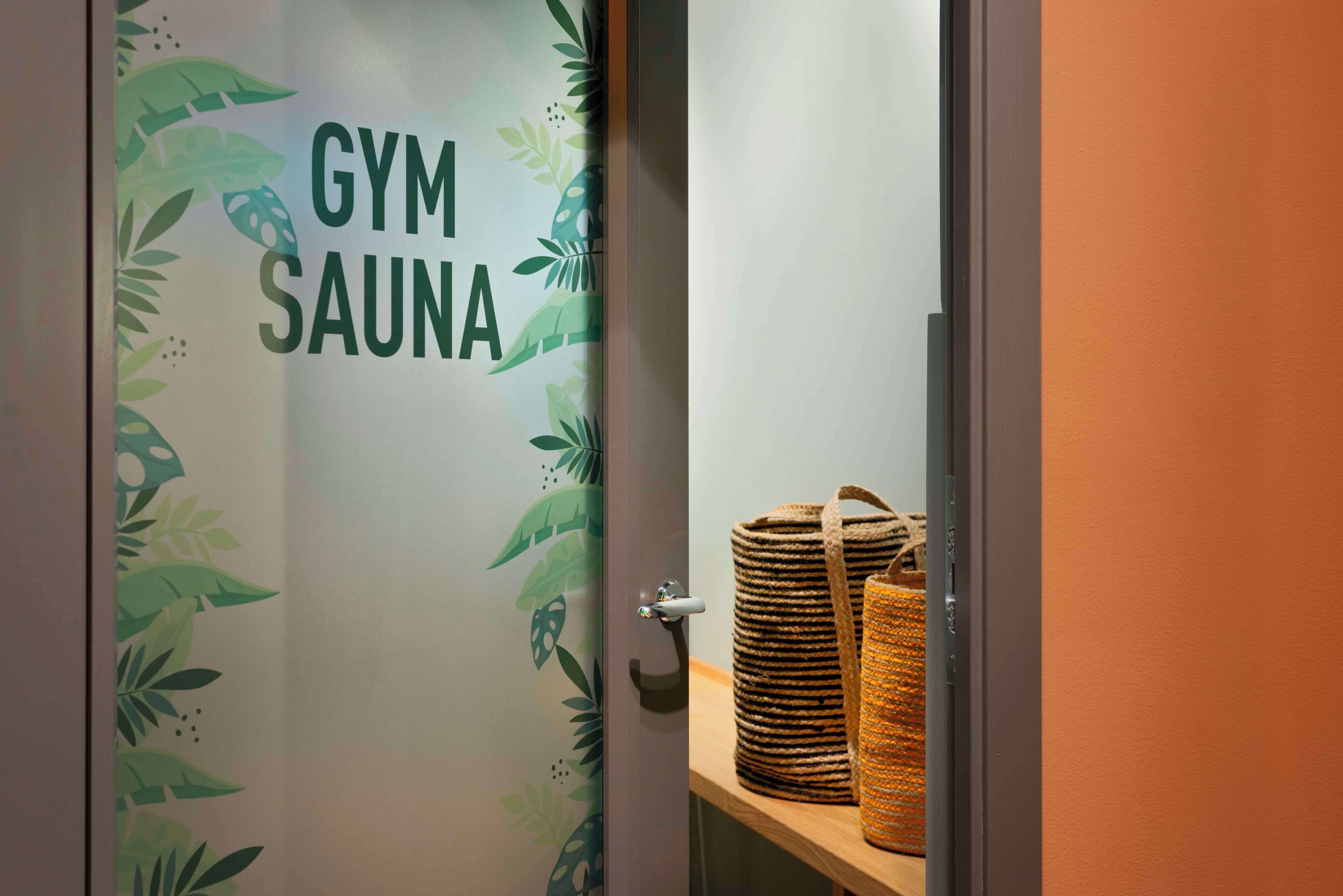 Ovi, jossa lukee »KUNTOSALI JA SAUNA», punottu kori ja puinen hylly.