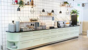 Une cuisine moderne avec des murs recouverts de carreaux blancs, un plan de travail vert clair et plusieurs luminaires suspendus.