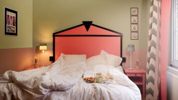 A neatly made bed with white bedding, a pink headboard, and a bedside table with a lamp and a vase of flowers.
