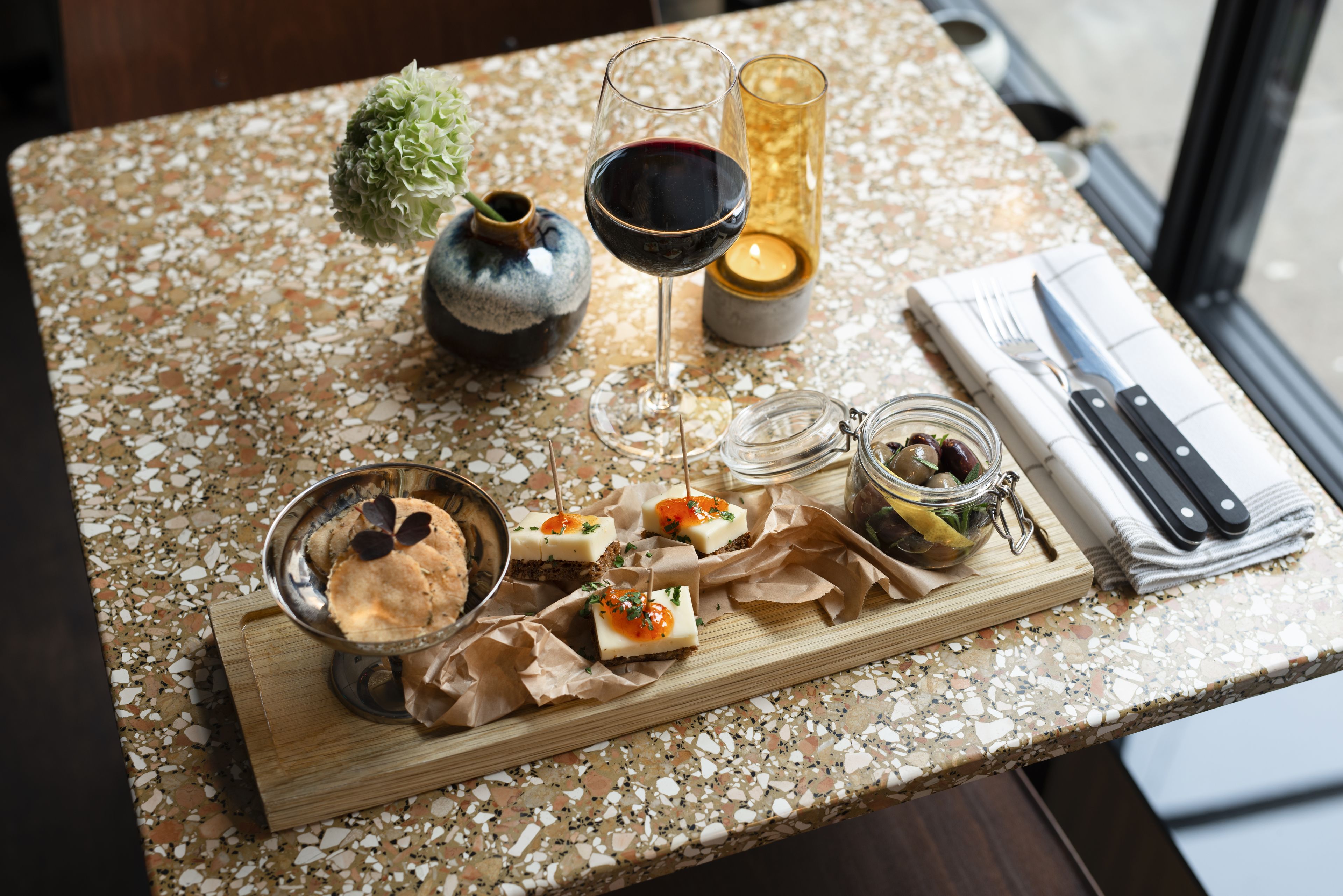 A table with a variety of food items, a glass of red wine, a candle, and a vase with a plant.