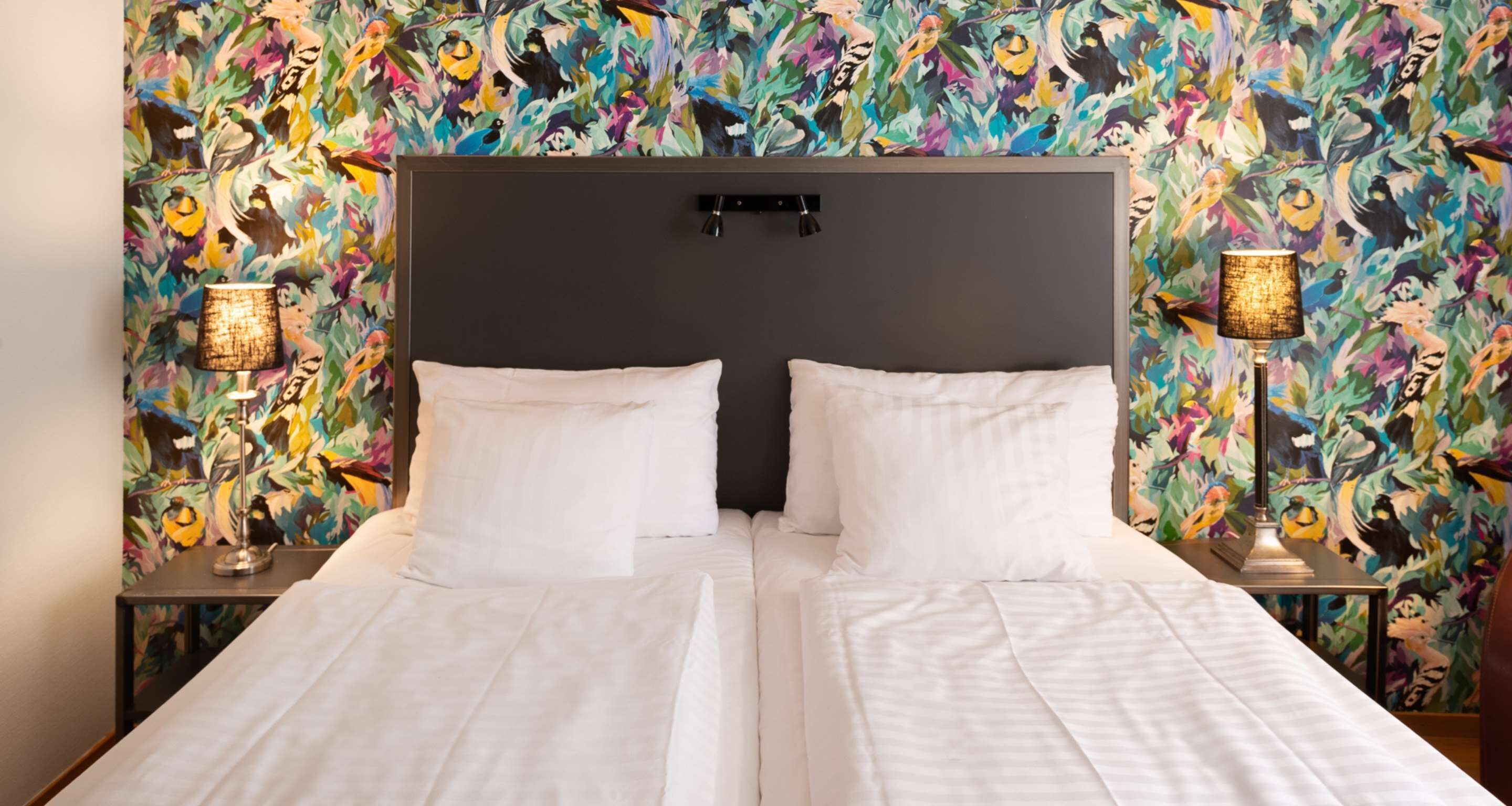 A double bed with white linens, a dark headboard, and two bedside lamps with patterned shades.