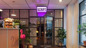 A hotel entrance with a 'SCRIPT' sign, glass doors, indoor plants, and a wooden reception desk. - Best Western Plus Hotel Noble House (Malmö)
