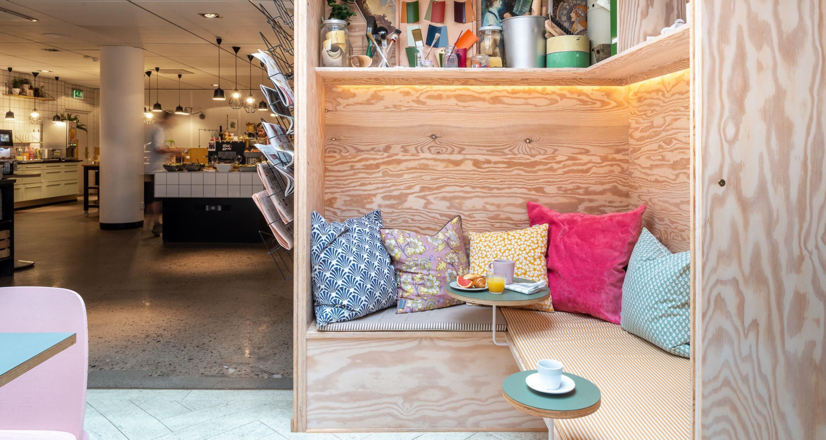 Un coin salon accueillant avec un banc en bois, des coussins et une petite table sur laquelle se trouvent une tasse et une soucoupe.