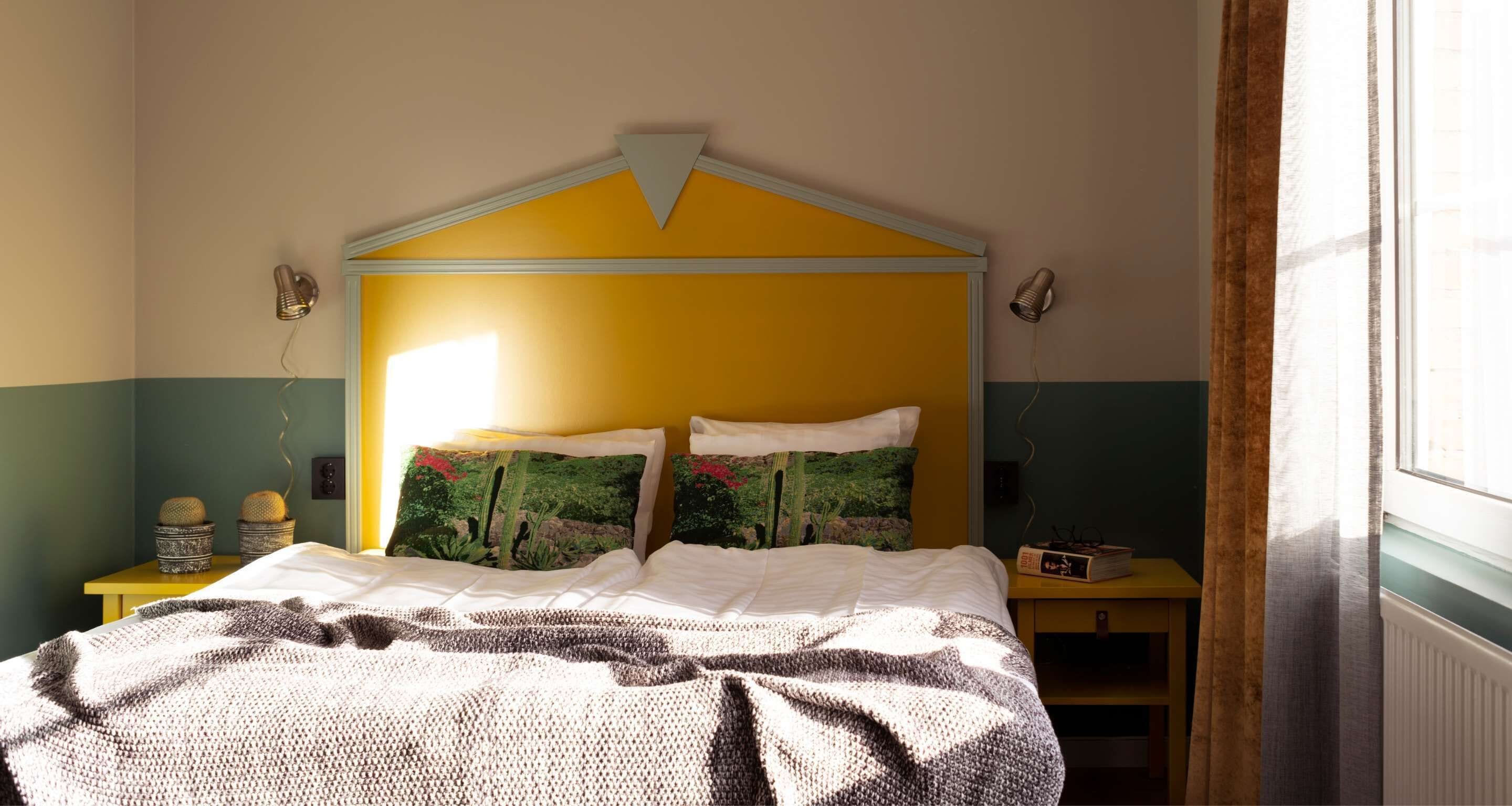 A bedroom with a bed, a nightstand, a lamp, and a window with curtains.