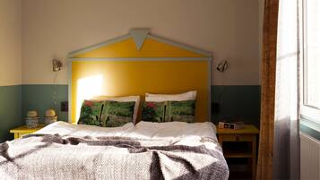 A bedroom with a bed, a nightstand, a lamp, and a window with curtains.