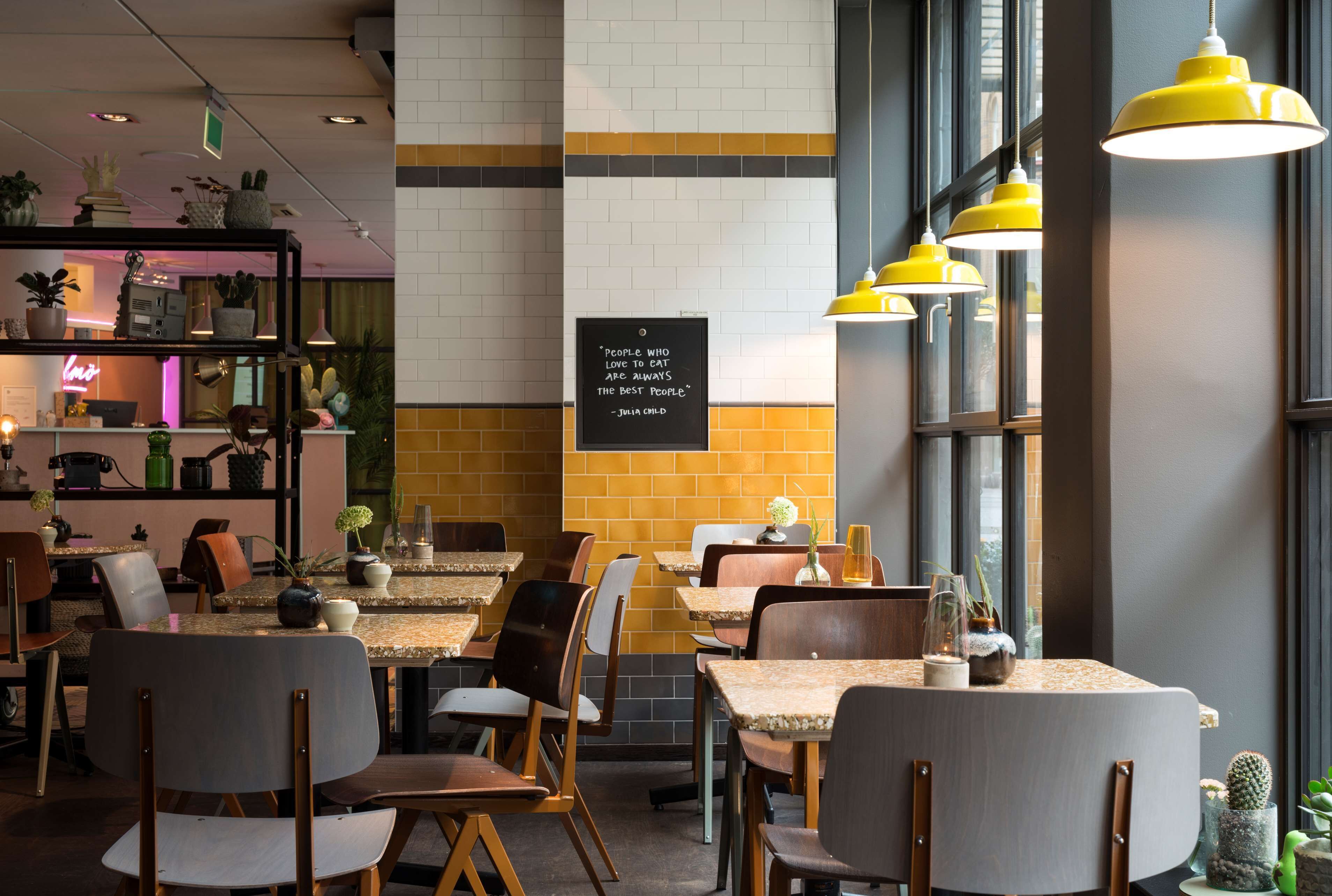 A cafe with tables and chairs, a shelf with plants, and a chalkboard with a quote.
