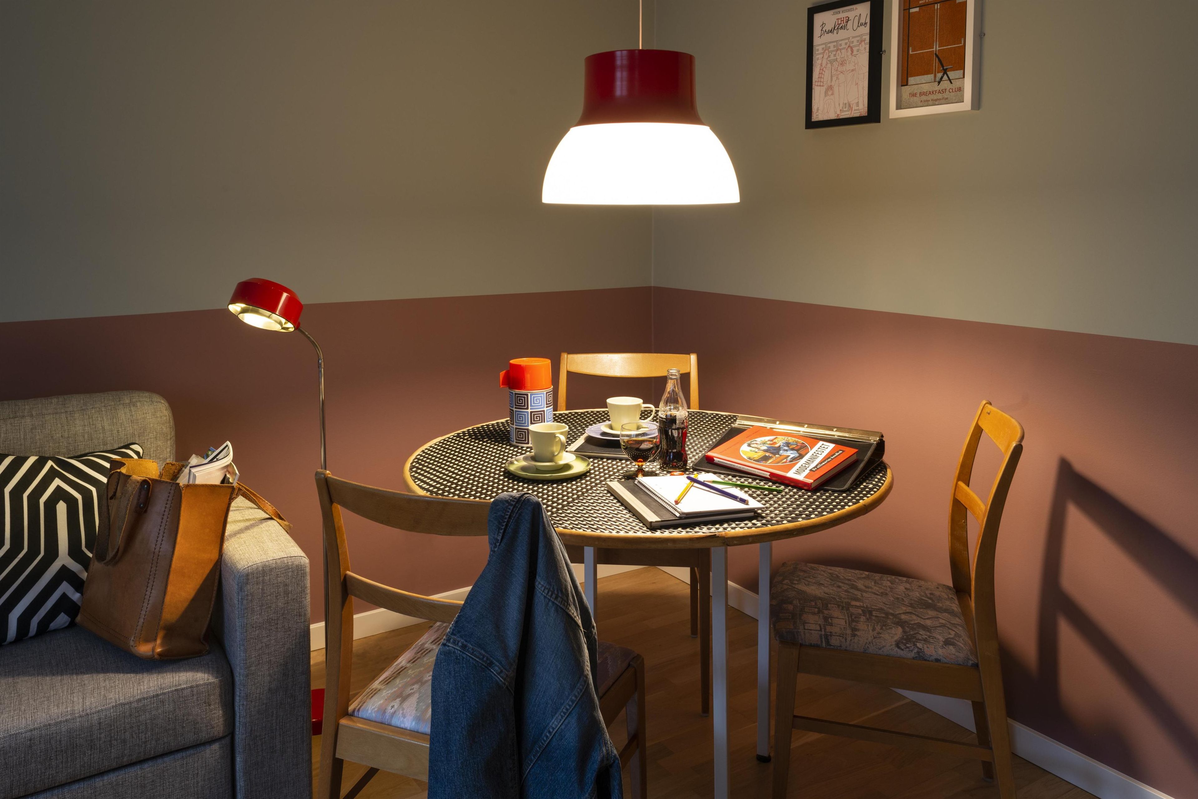 A cozy corner with a round table, chairs, a lamp, and a wall with framed pictures.