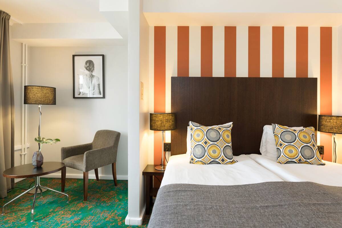 A hotel room with a bed, a chair, a table, and a lamp.