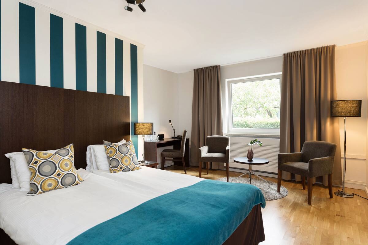 A hotel room with a large bed, two armchairs, a desk, and a window with curtains.