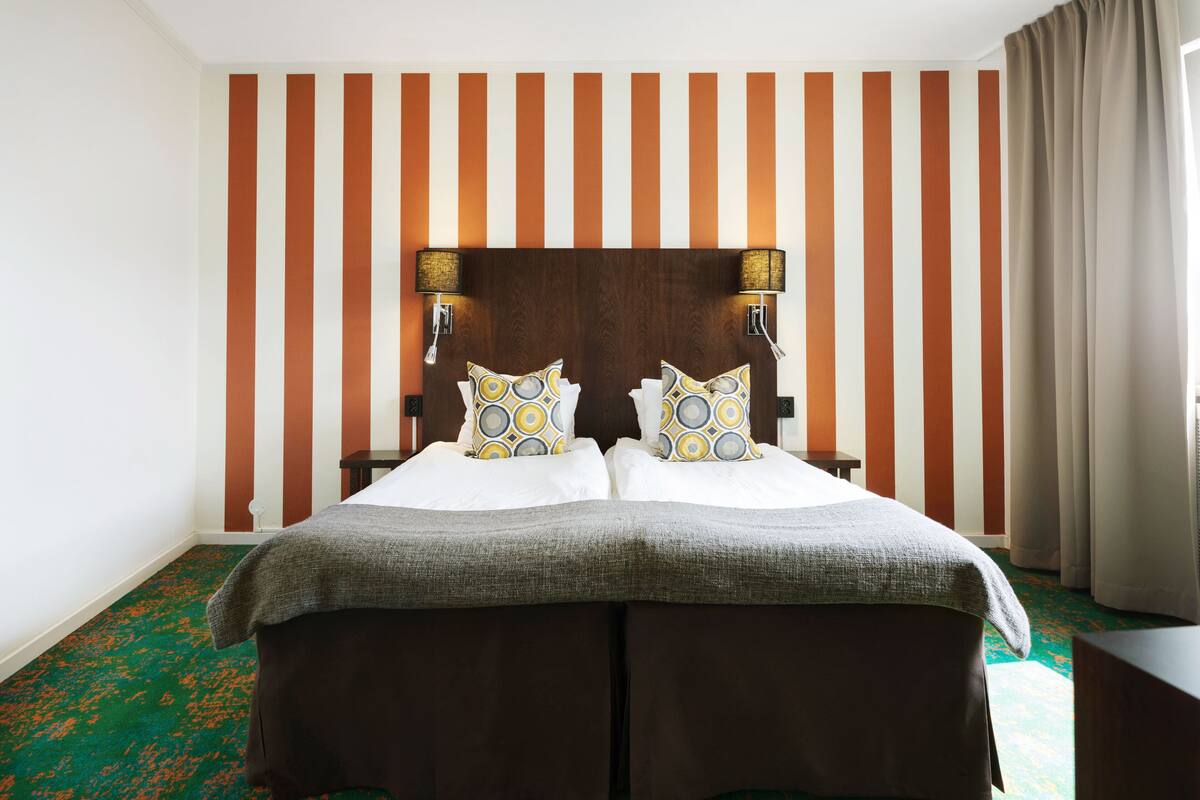 A double bed with a headboard, two wall-mounted lamps, and patterned pillows.