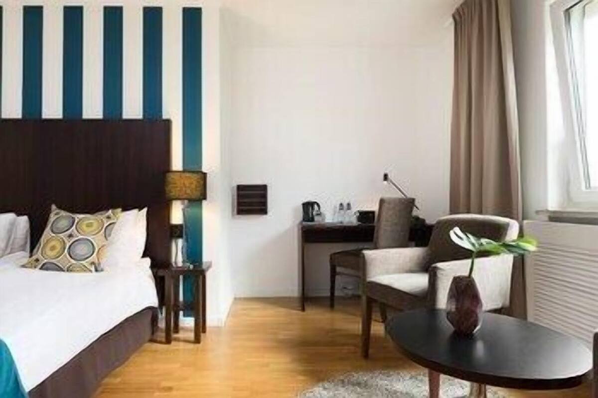 A hotel room with a bed, a desk, a chair, and a small table.