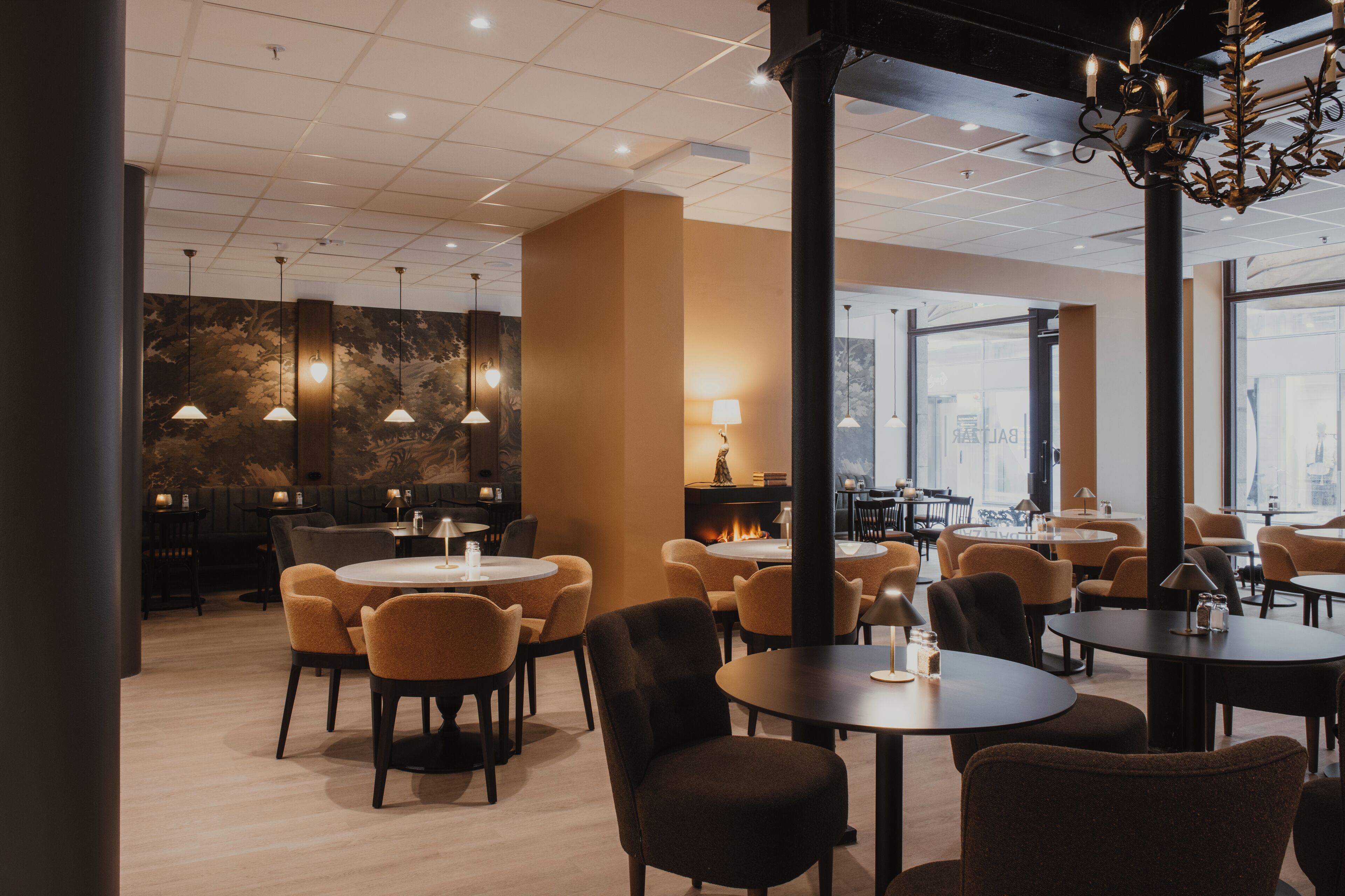 A modern dining area with round tables and chairs, pendant lighting, and a fireplace.