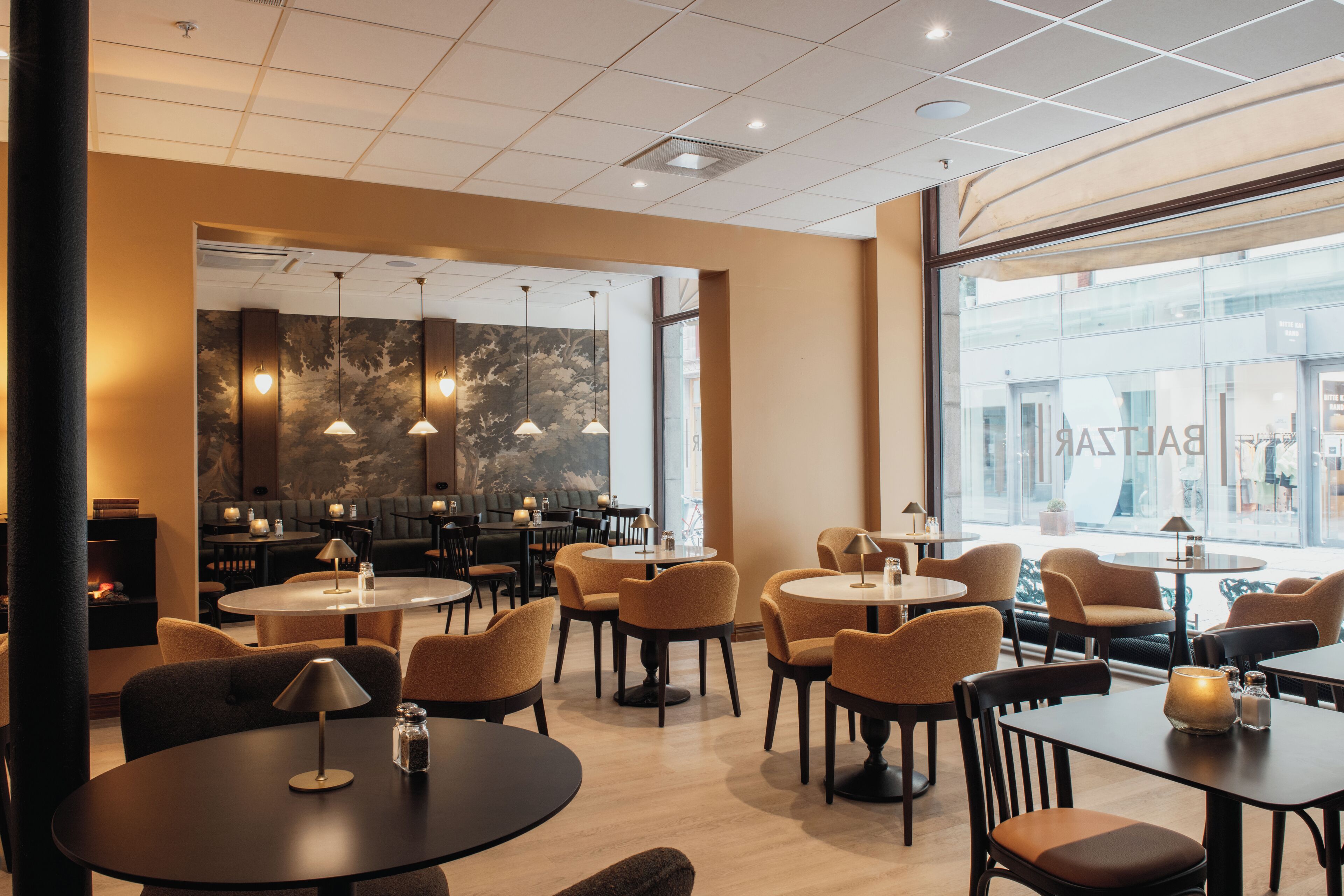 Un interno ristorante moderno con tavoli rotondi, sedie imbottite, luci a sospensione e un'ampia vetrata che si affaccia sulla strada.