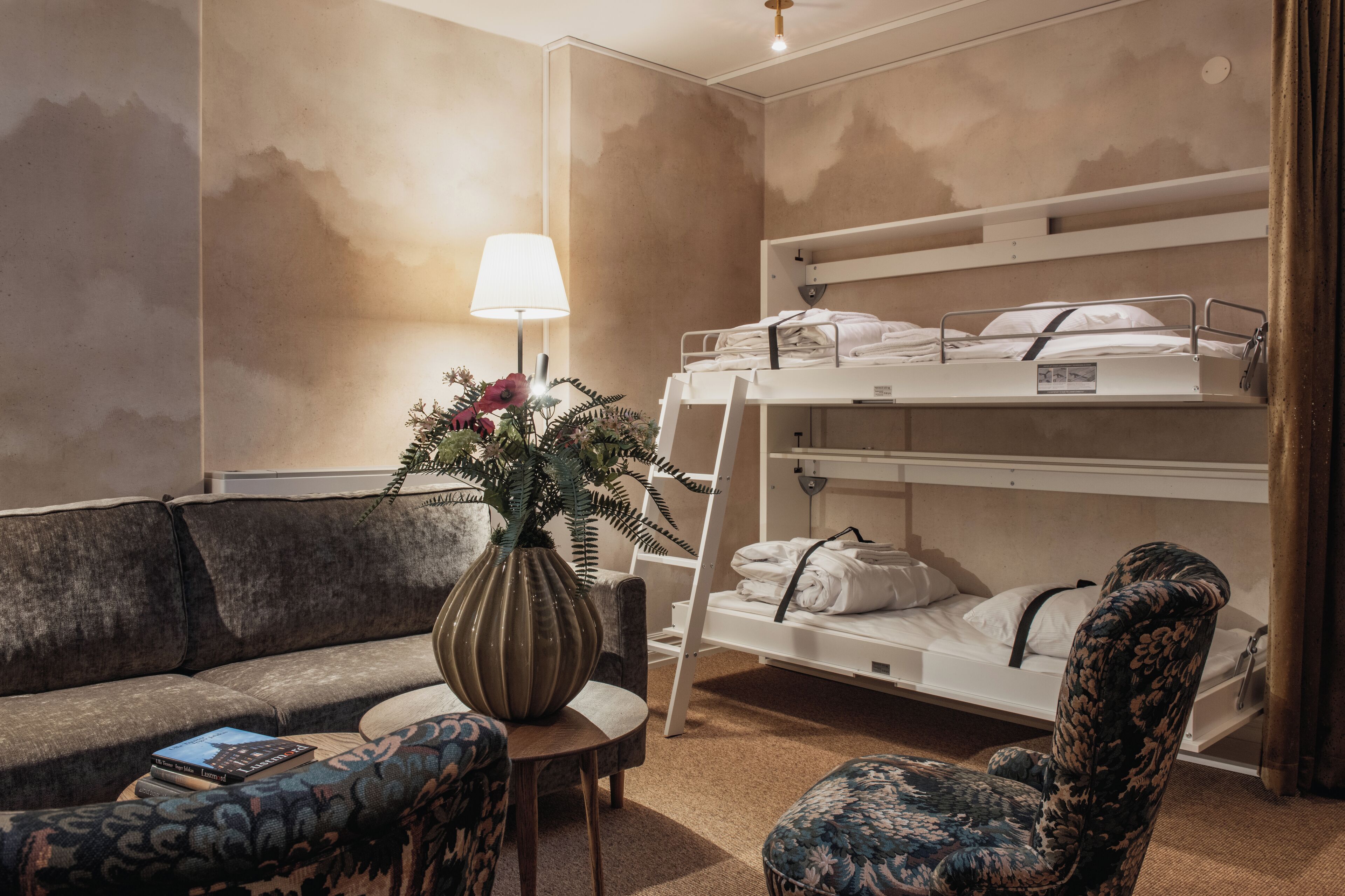Una habitación de hotel con literas, un sofá, una mesita y una lámpara.