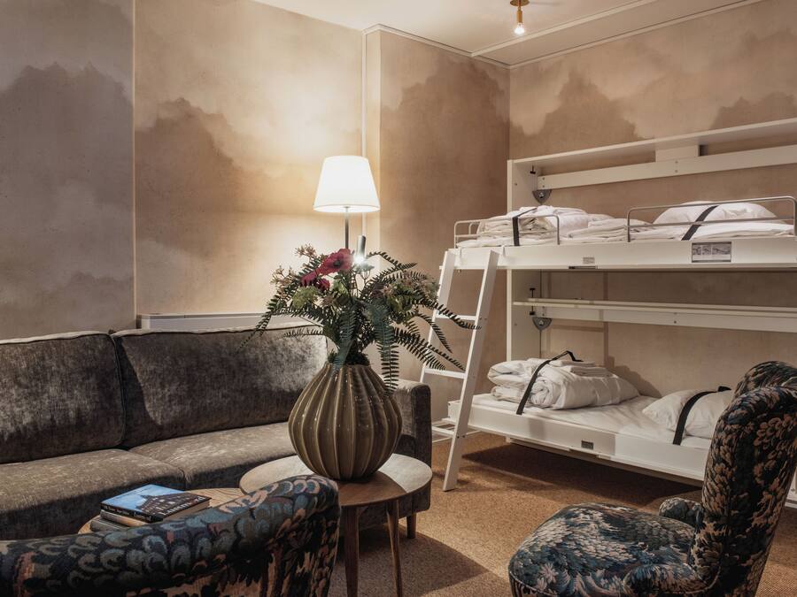 Una habitación de hotel con literas, un sofá, una mesita y una lámpara.