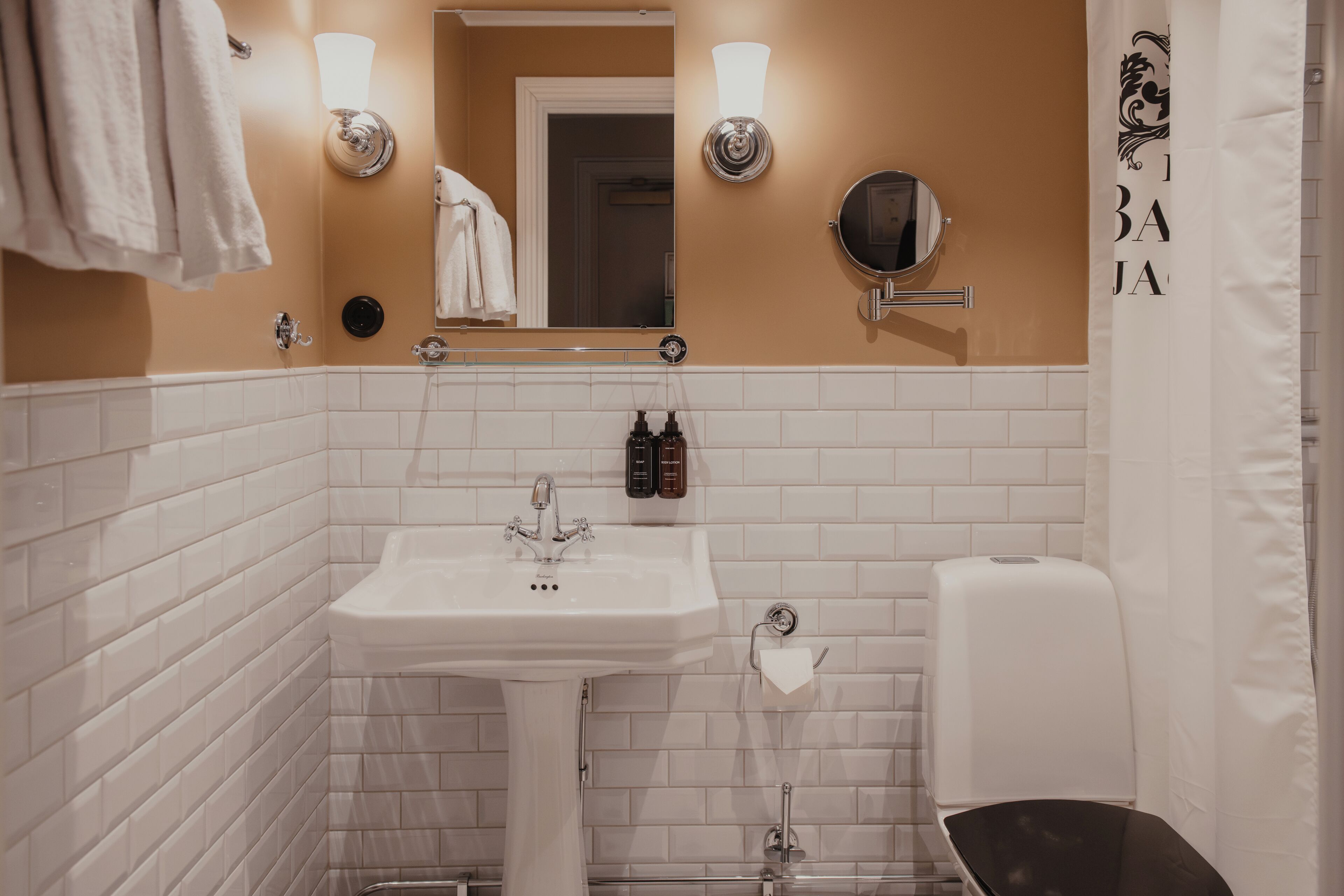 A bathroom with a white sink, two wall-mounted light fixtures, a mirror, and a towel rack.