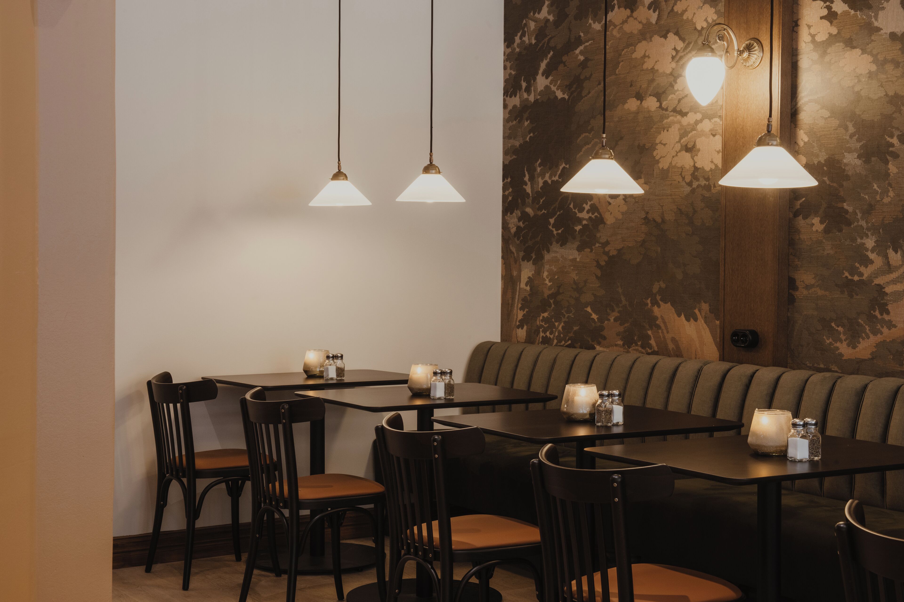 A dining area with tables and chairs, a sofa, and hanging pendant lights.