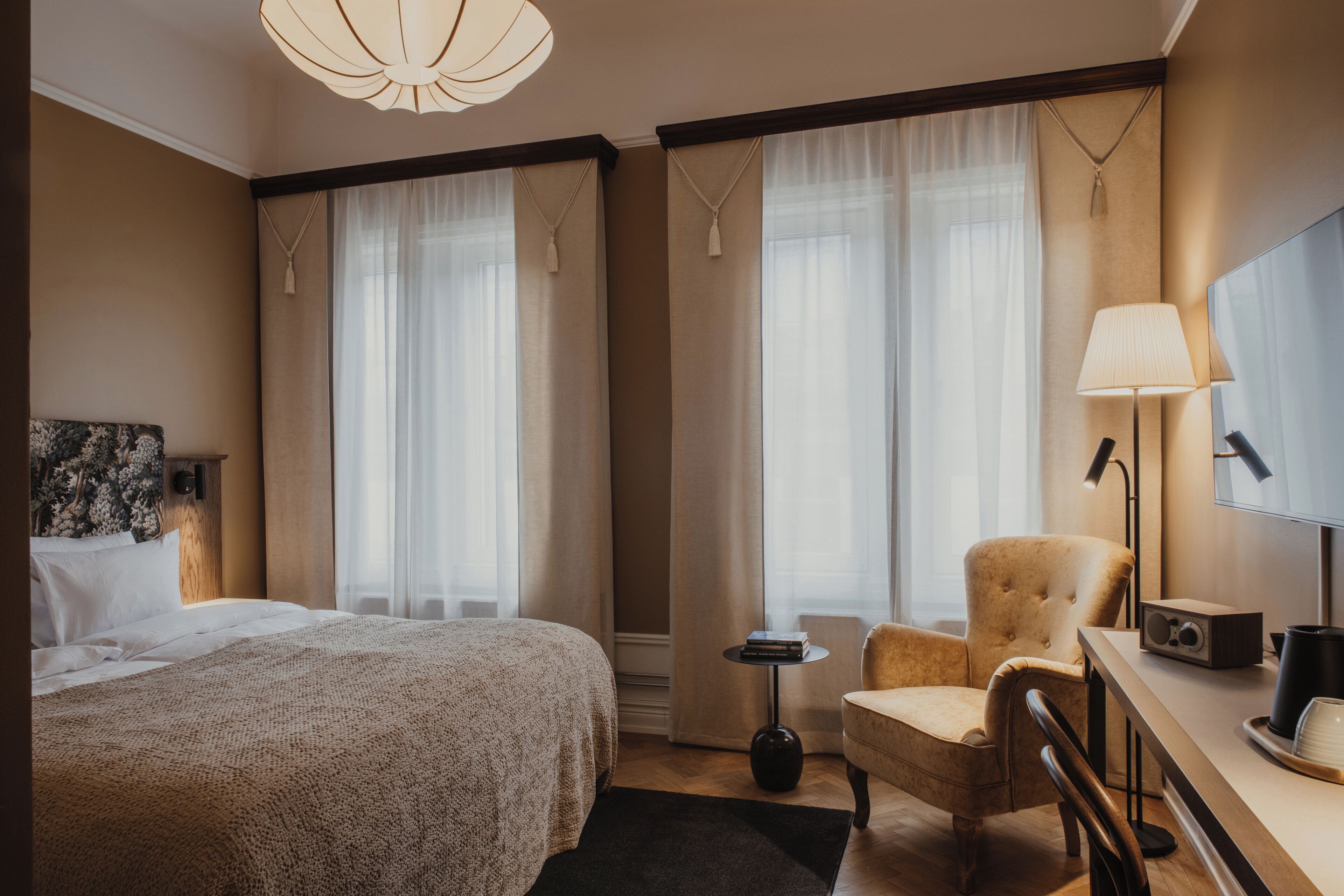 Ett hotellrum med en stor säng, en stol, ett skrivbord med en lampa och en tv.